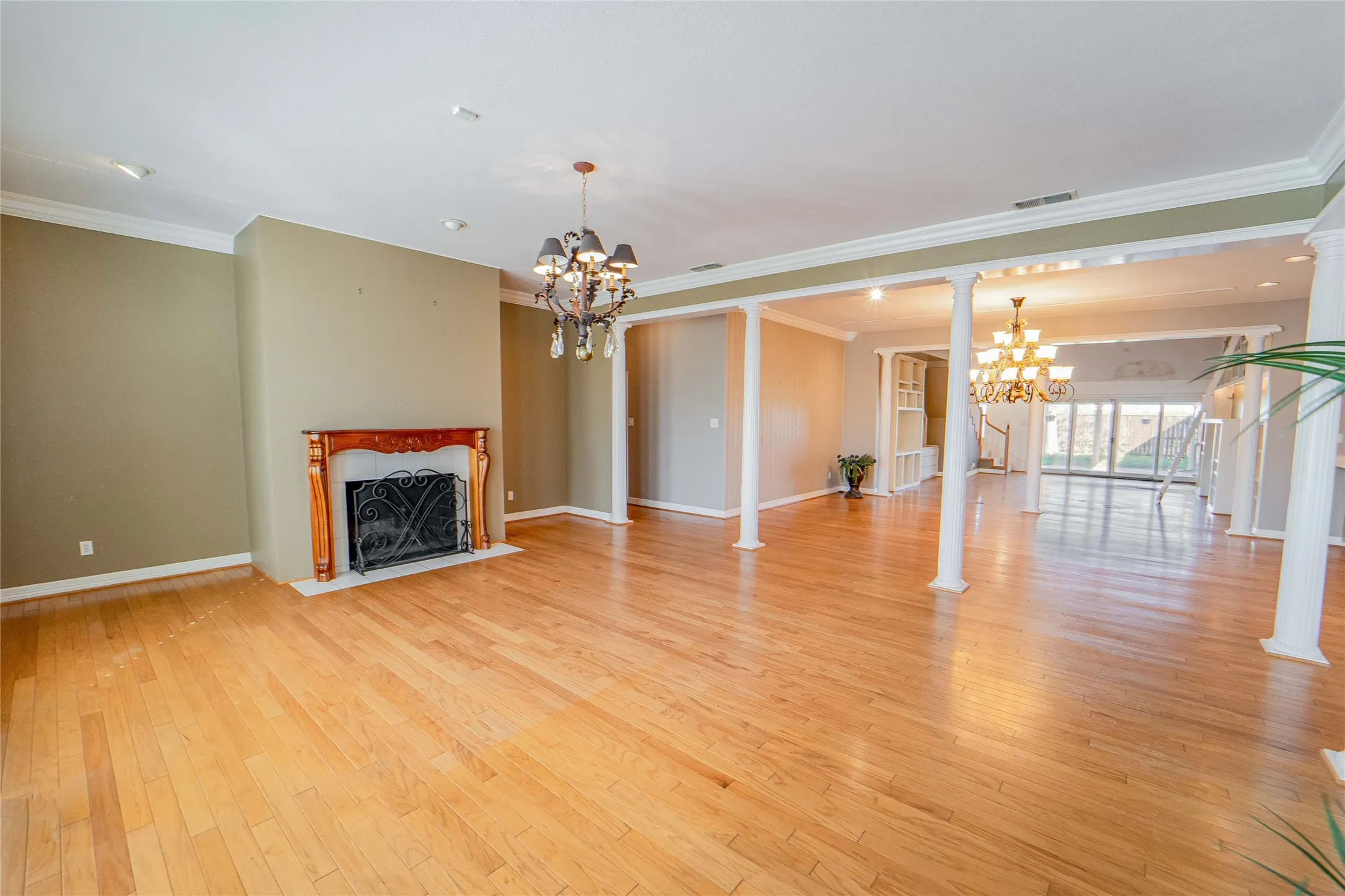 Living room with hanging lights, crown molding, light wood-type flooring, a fireplace with flush hearth, and ornate columns