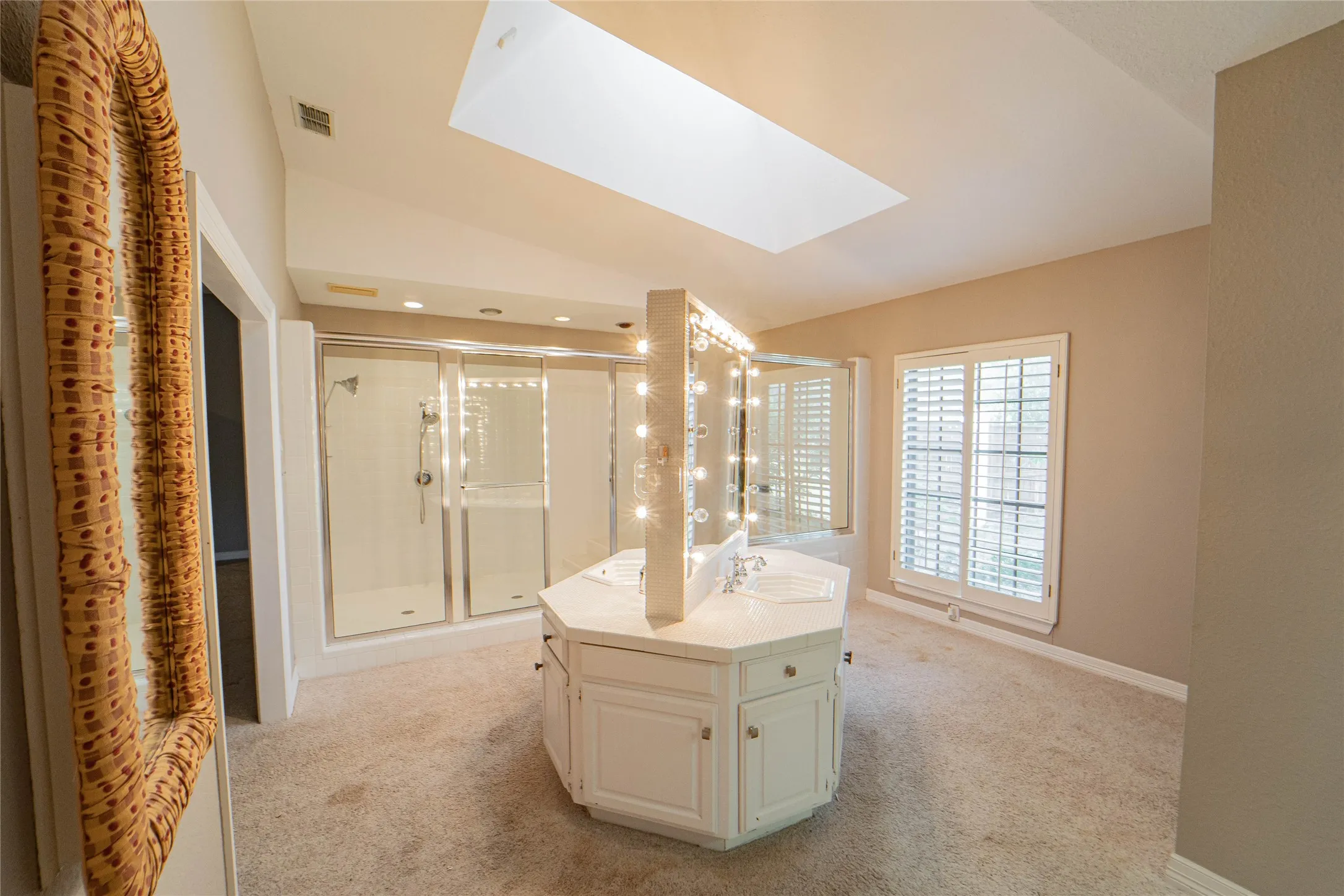 Full bathroom featuring vaulted ceiling, a skylight, light colored carpet, vanity, and a shower stall