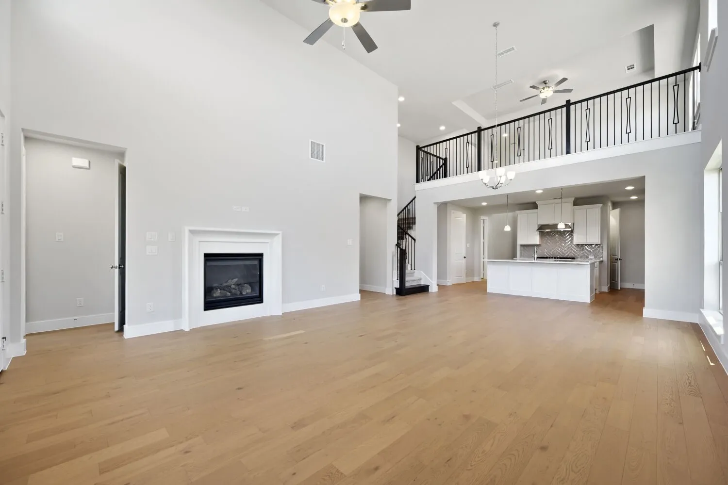 Open-concept living area with soaring ceilings, wood-finish flooring, and a white mantle fireplace