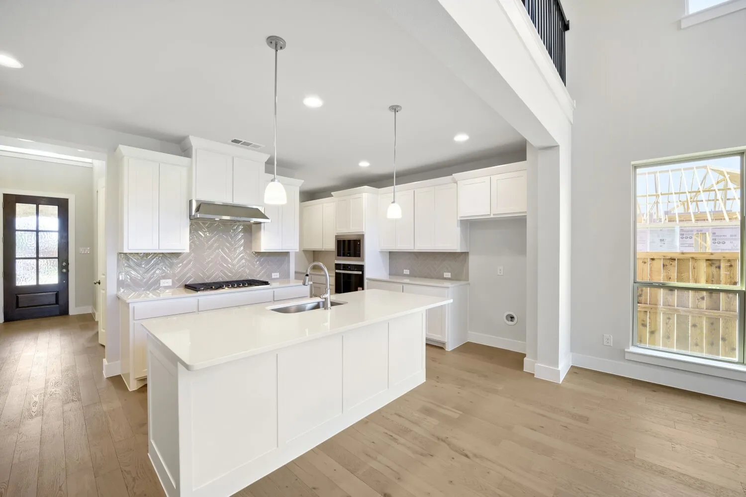 Modern kitchen featuring white cabinetry, a large center island with a sink, stainless steel appliances, and a herringbone tile backsplash