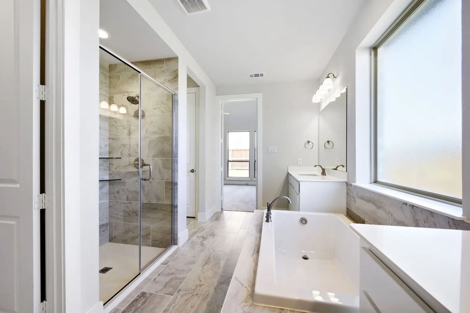 Spacious bathroom featuring a glass-enclosed shower, a built-in soaking tub, dual vanities with white countertops, and wood-finish tile flooring
