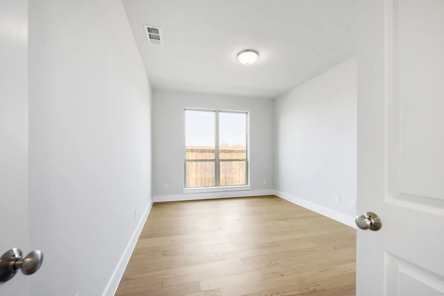 Spacious room featuring light wood-finish flooring, a large window, white walls, white trim, and a ceiling-mounted light fixture