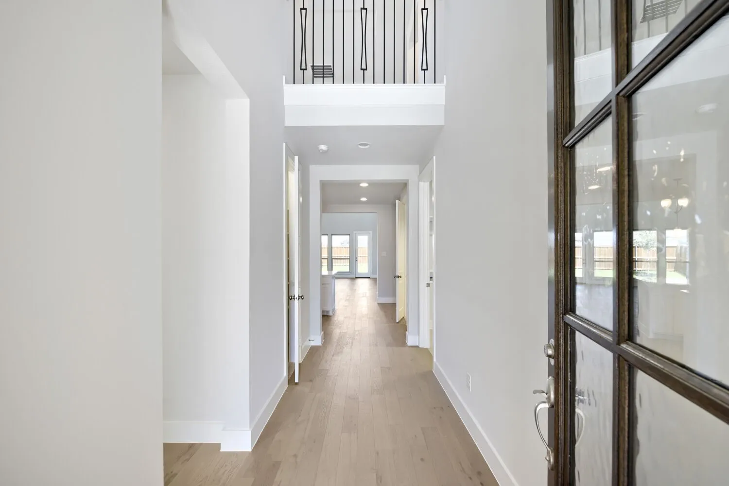 Entryway featuring wood-finish flooring extending throughout, a dark-framed glass paneled door, recessed lighting, and a second-story balcony with decorative metal railings