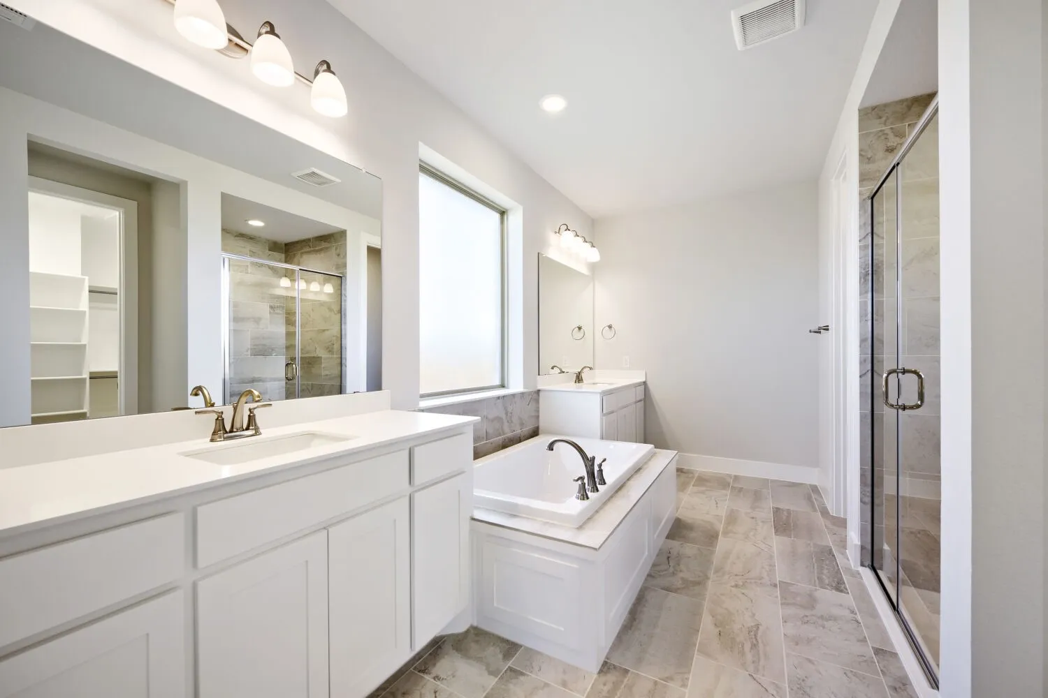Bathroom featuring a built-in soaking tub, a frameless glass shower enclosure, and two distinct vanity stations with integrated sinks and white cabinetry