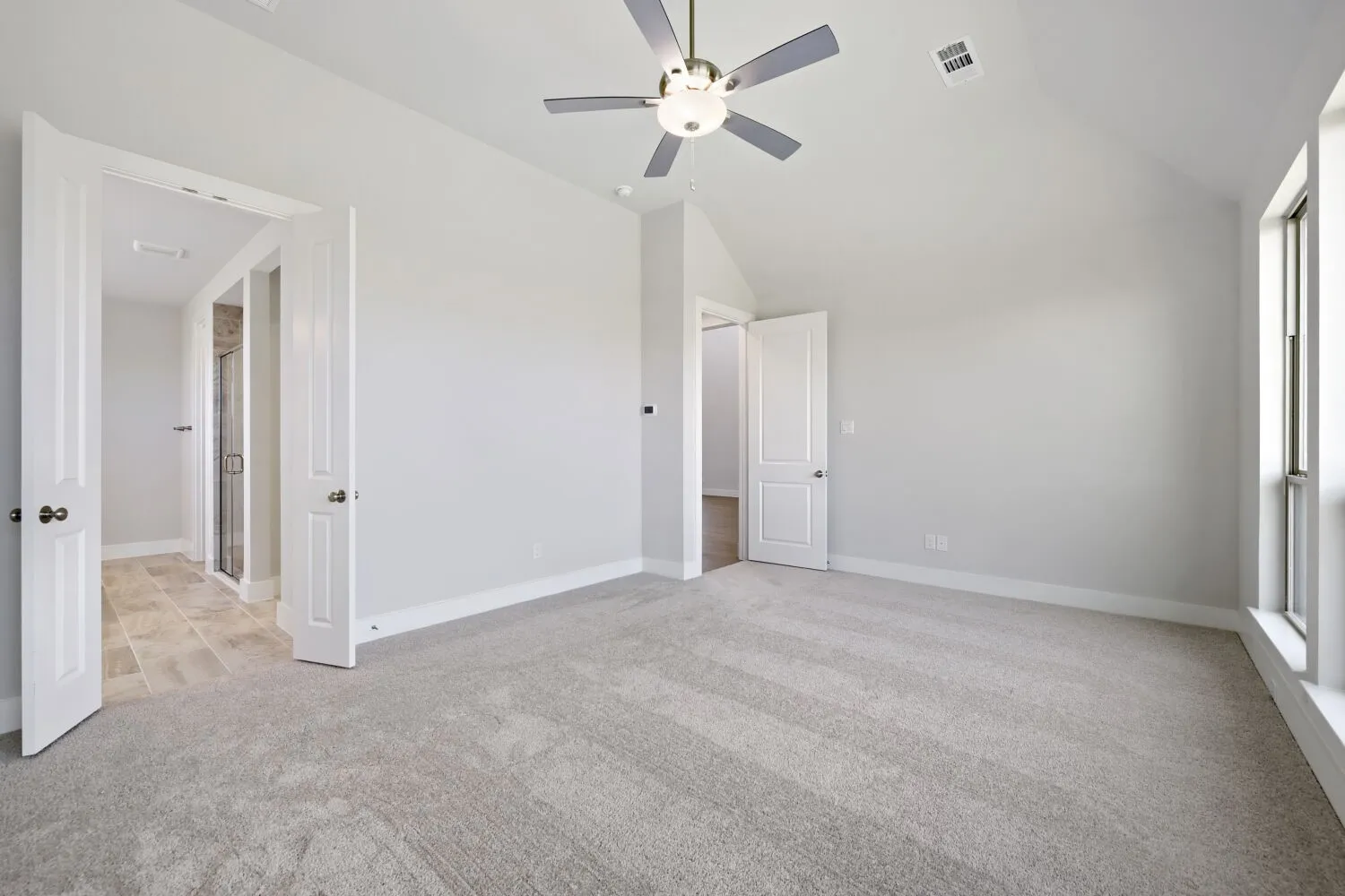 Carpeted room featuring a vaulted ceiling with a ceiling fan, a window, and two doorways