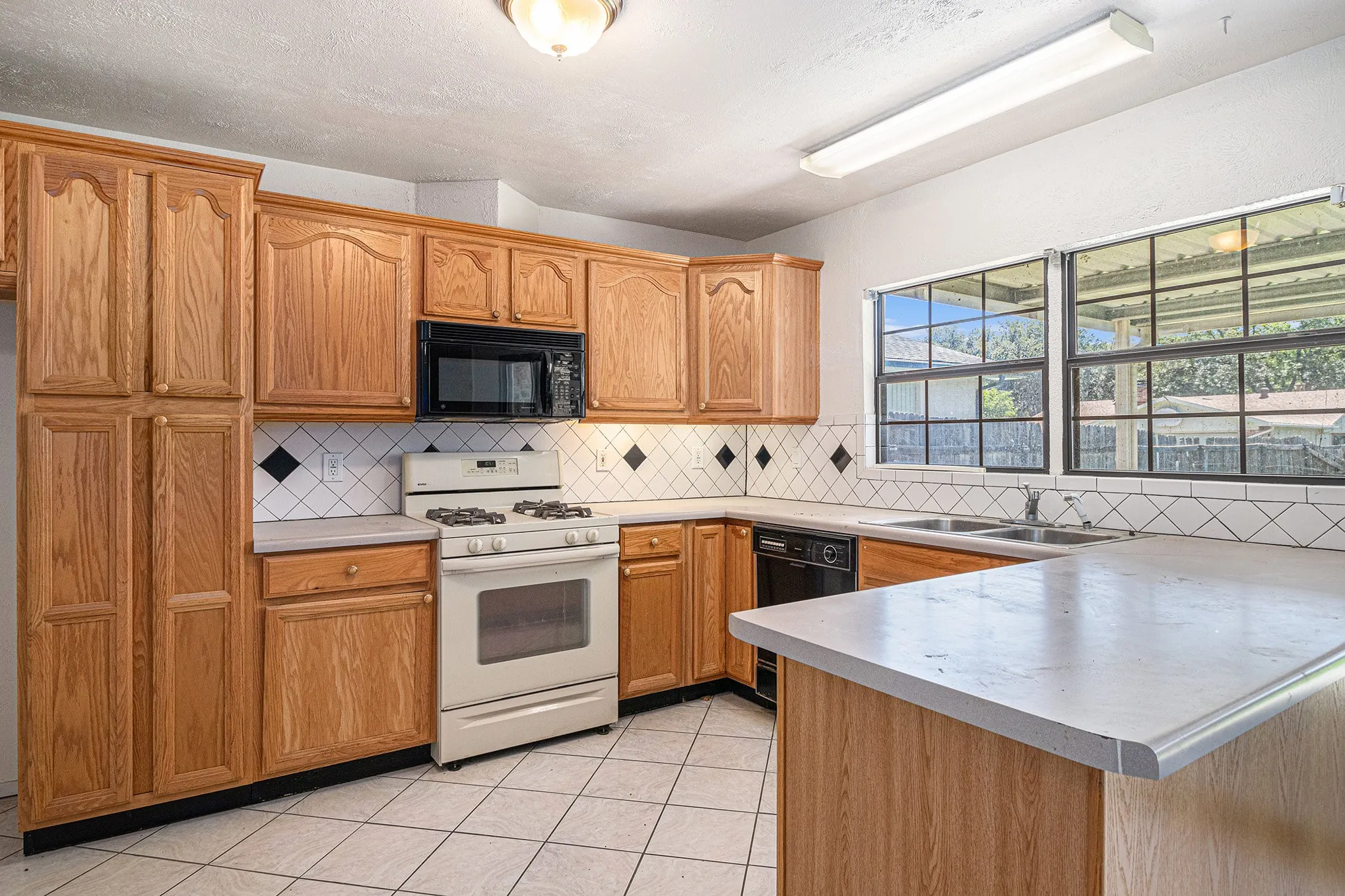 Kitchen with light tile floors, kitchen peninsula, black appliances, backsplash, and sink