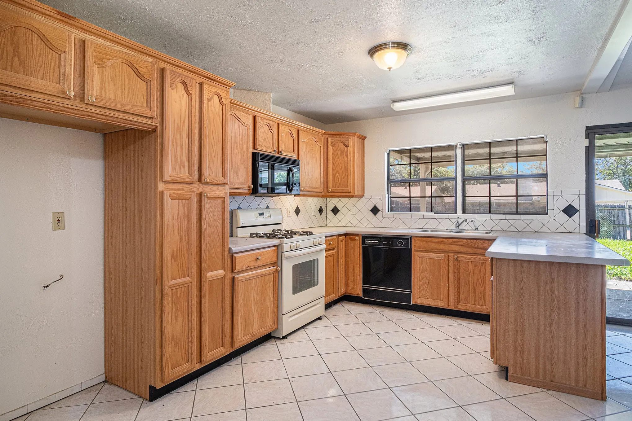 Kitchen with light tile flooring, a textured ceiling, black appliances, backsplash, and sink