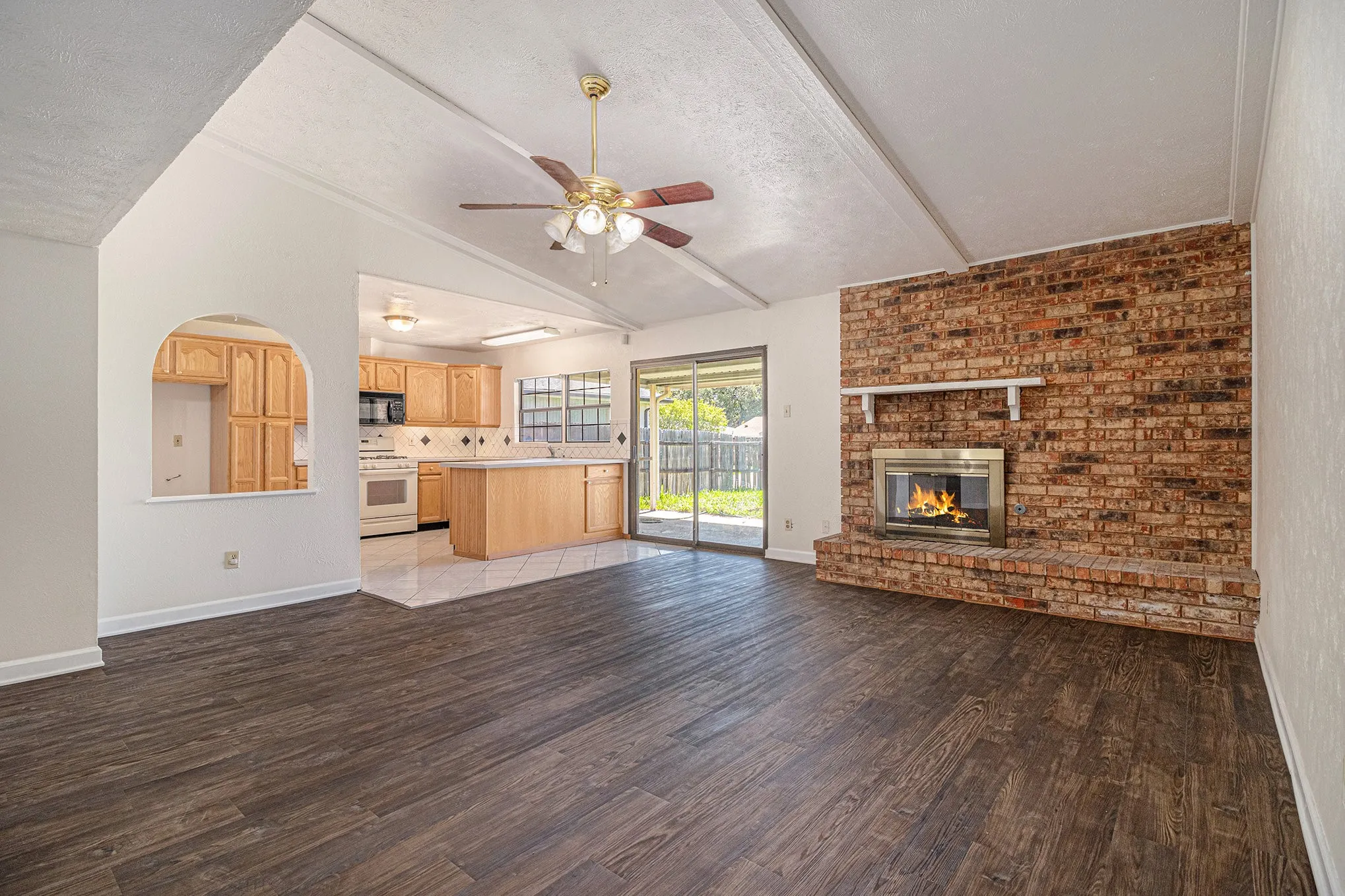 Unfurnished living room with hardwood / wood-style flooring, a fireplace, ceiling fan, a textured ceiling, and vaulted ceiling