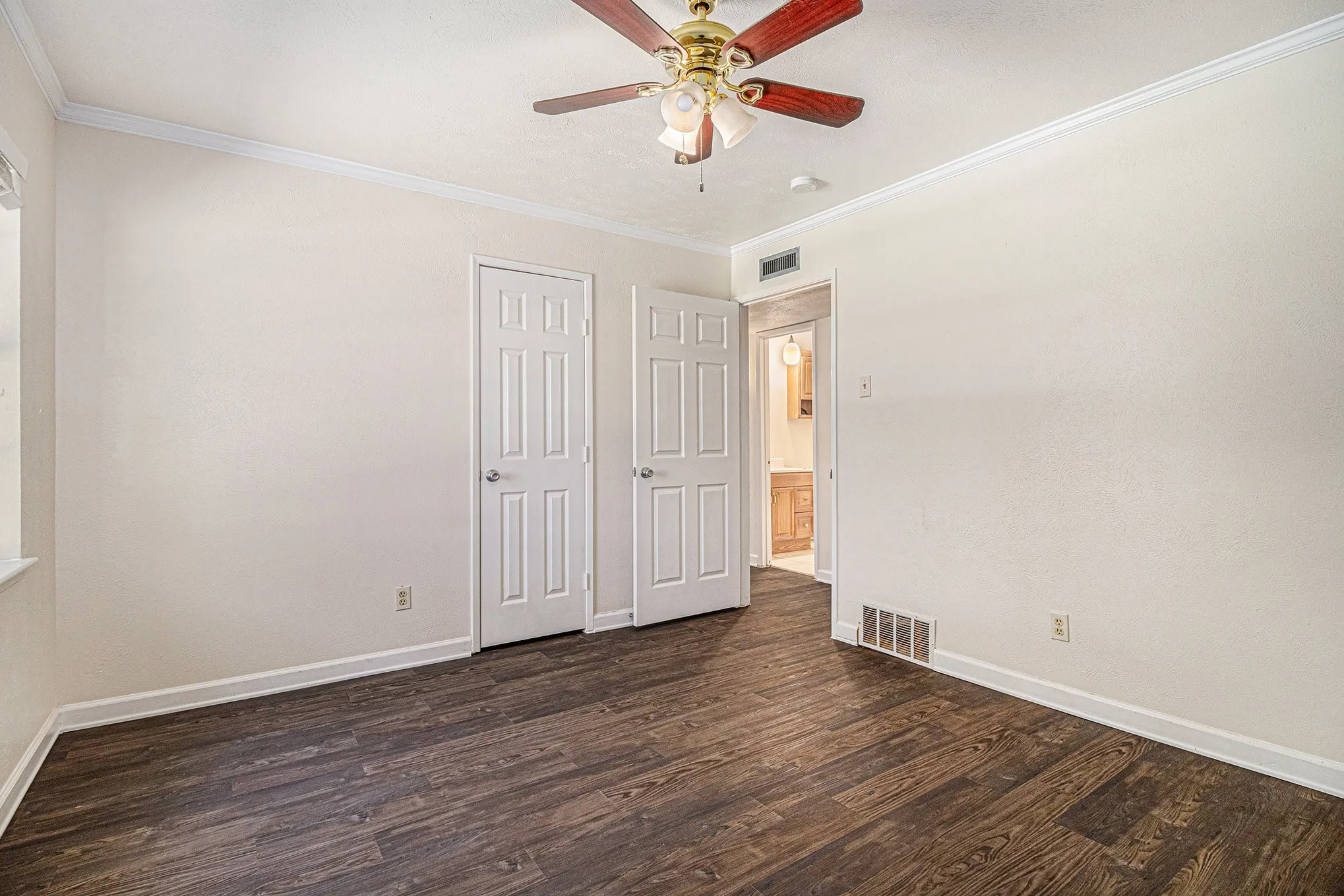 Empty room with dark hardwood / wood-style floors, ornamental molding, and ceiling fan