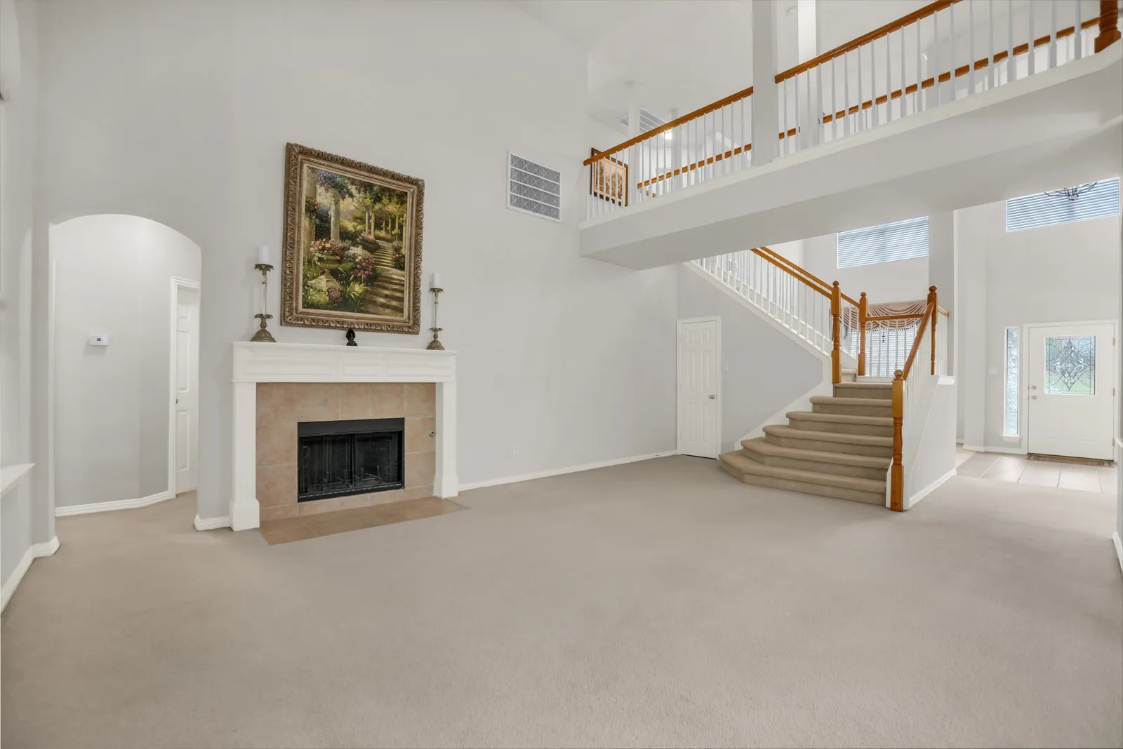 Unfurnished living room with a high ceiling, arched walkways, a tile fireplace, and light carpet