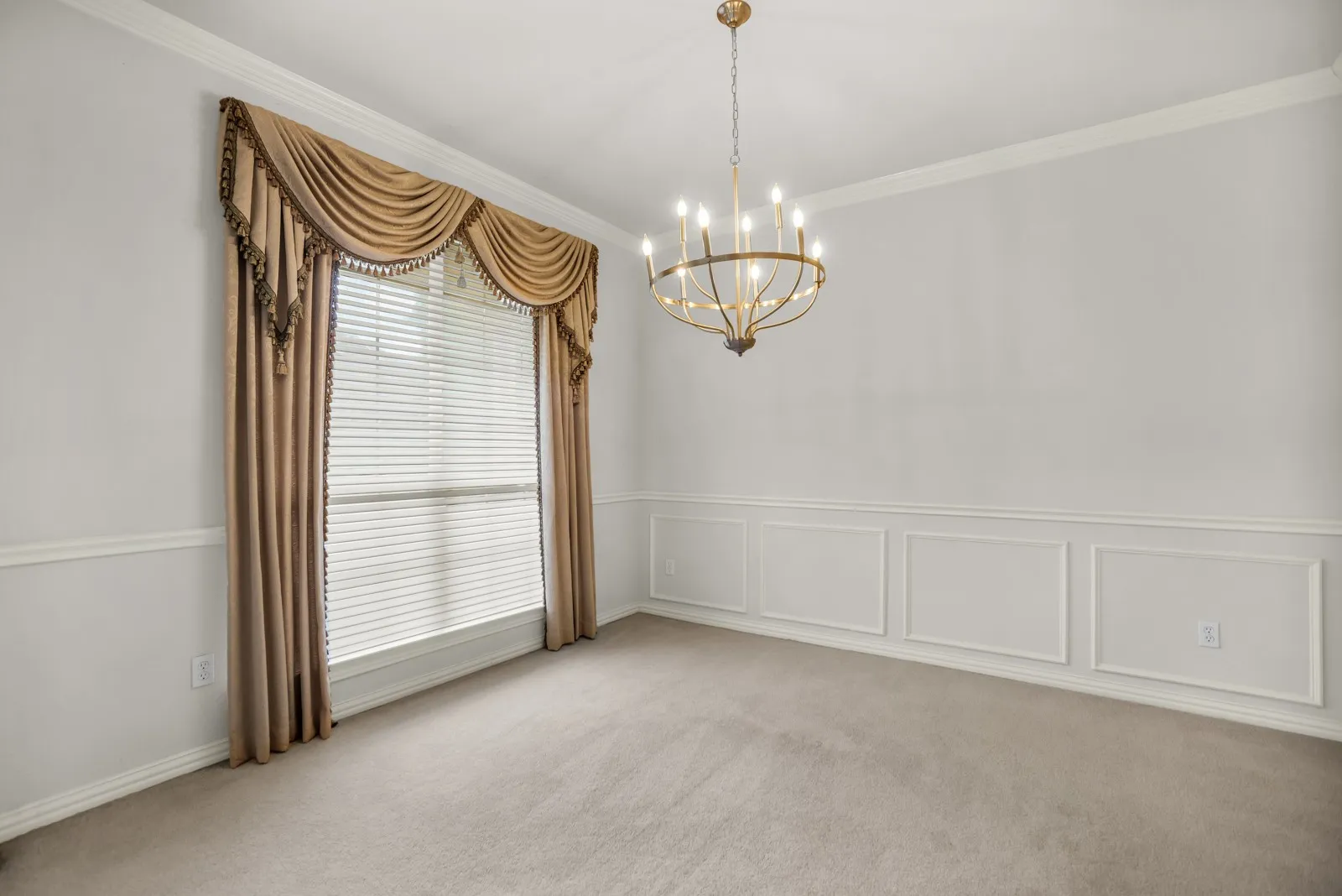 Unfurnished room with crown molding, a chandelier, light colored carpet, a wainscoted wall, and a decorative wall