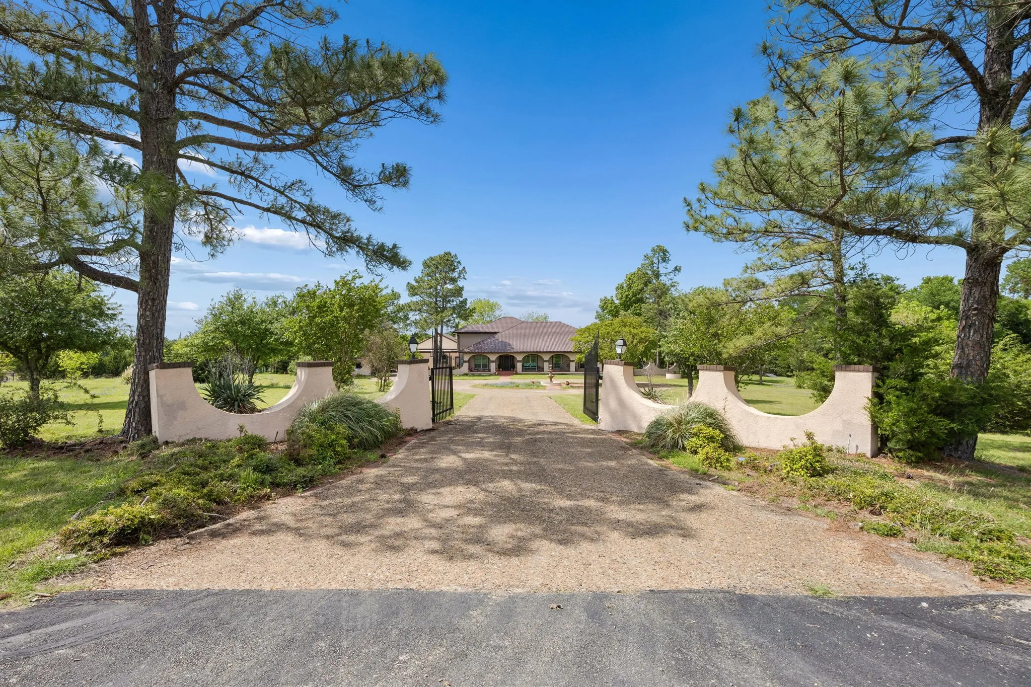 Gated entry with a gravel driveway, mature trees, and YOUR HOME!!