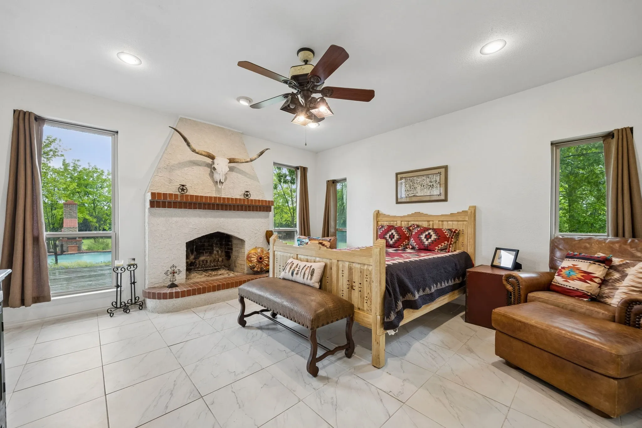 Spacious room featuring a white tile floor, a prominent fireplace with a red brick hearth and mantel, multiple windows, recessed lighting, and a ceiling fan