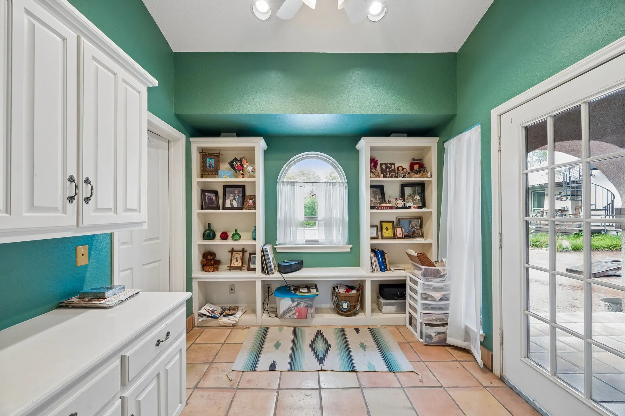 Built-in shelving flanking an arched window, with terracotta tile flooring and a French patio door