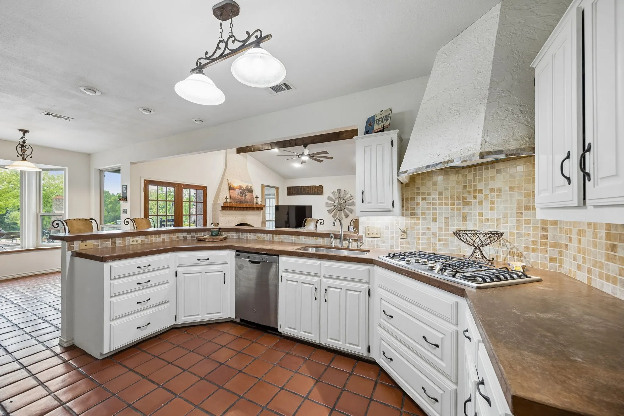 Kitchen featuring terracotta tile flooring, white cabinetry with dark hardware, a built-in gas range, a mosaic tile backsplash, and a custom range hood