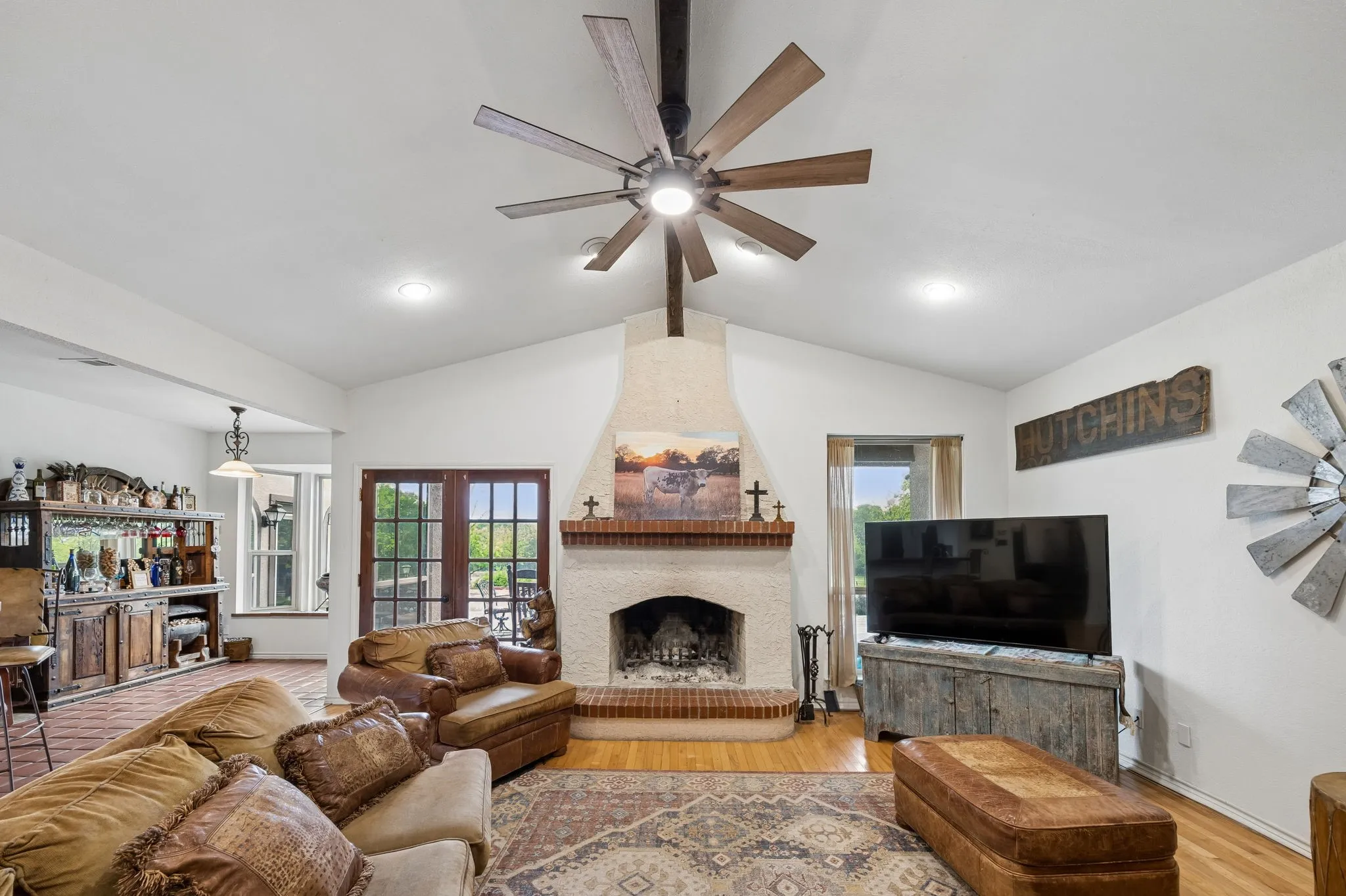 Spacious living area featuring a vaulted ceiling with a large ceiling fan, a stucco fireplace with a brick hearth and mantel, and wood-finish flooring