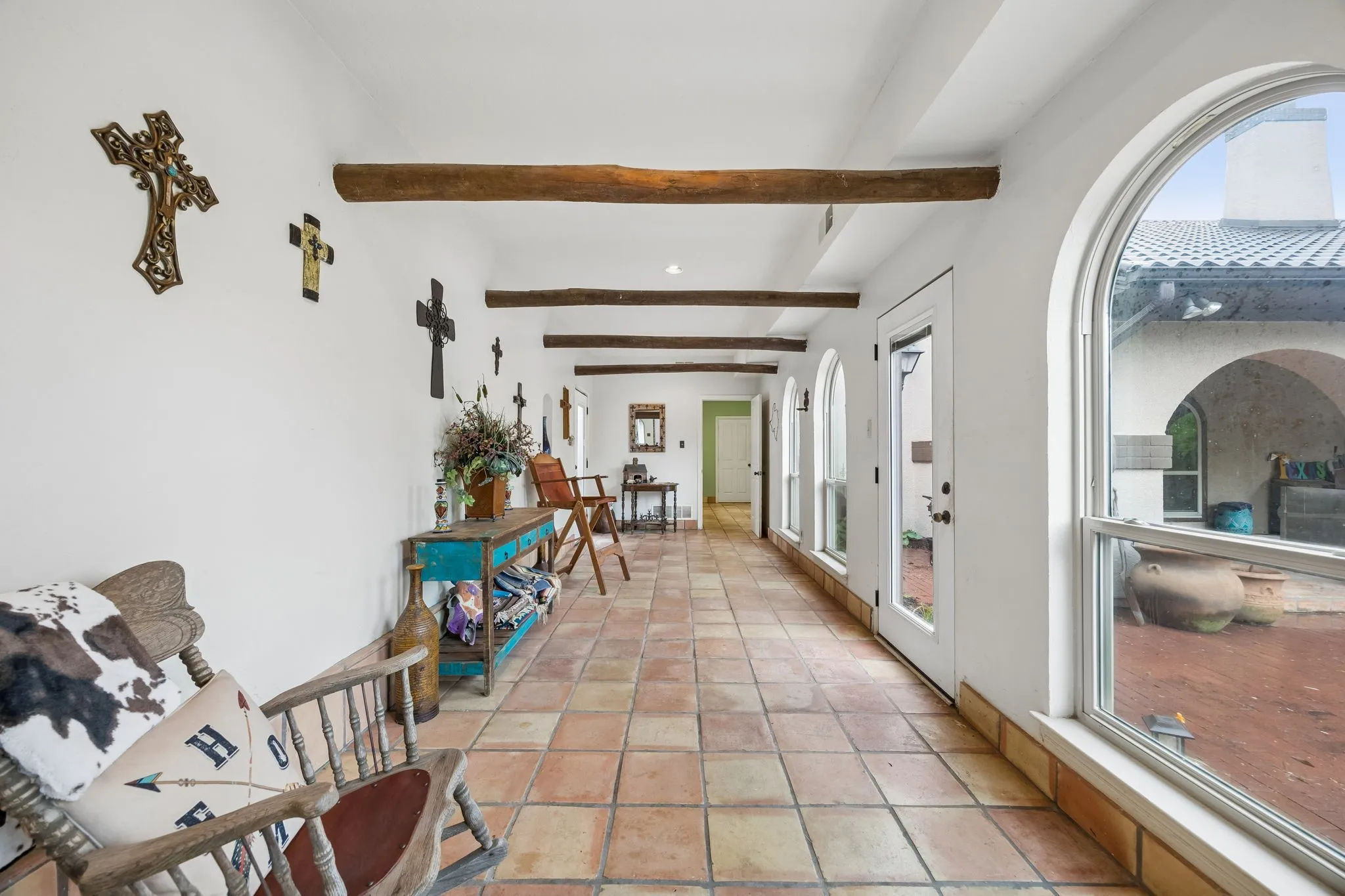 Hallway featuring terracotta tile flooring, exposed wood beams, multiple arched windows, and arched glass-panel doors