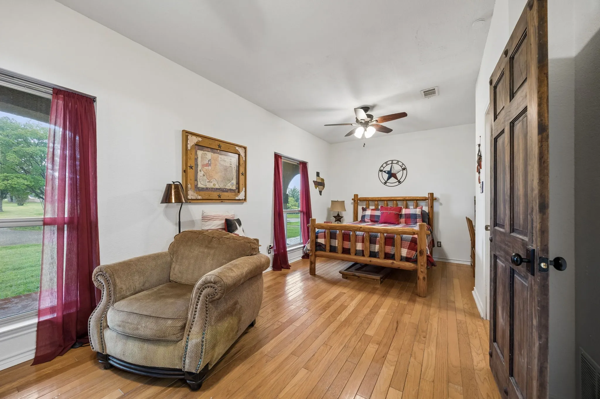 Hardwood flooring extends throughout this room, featuring multiple windows, a ceiling fan, and a wood-paneled door