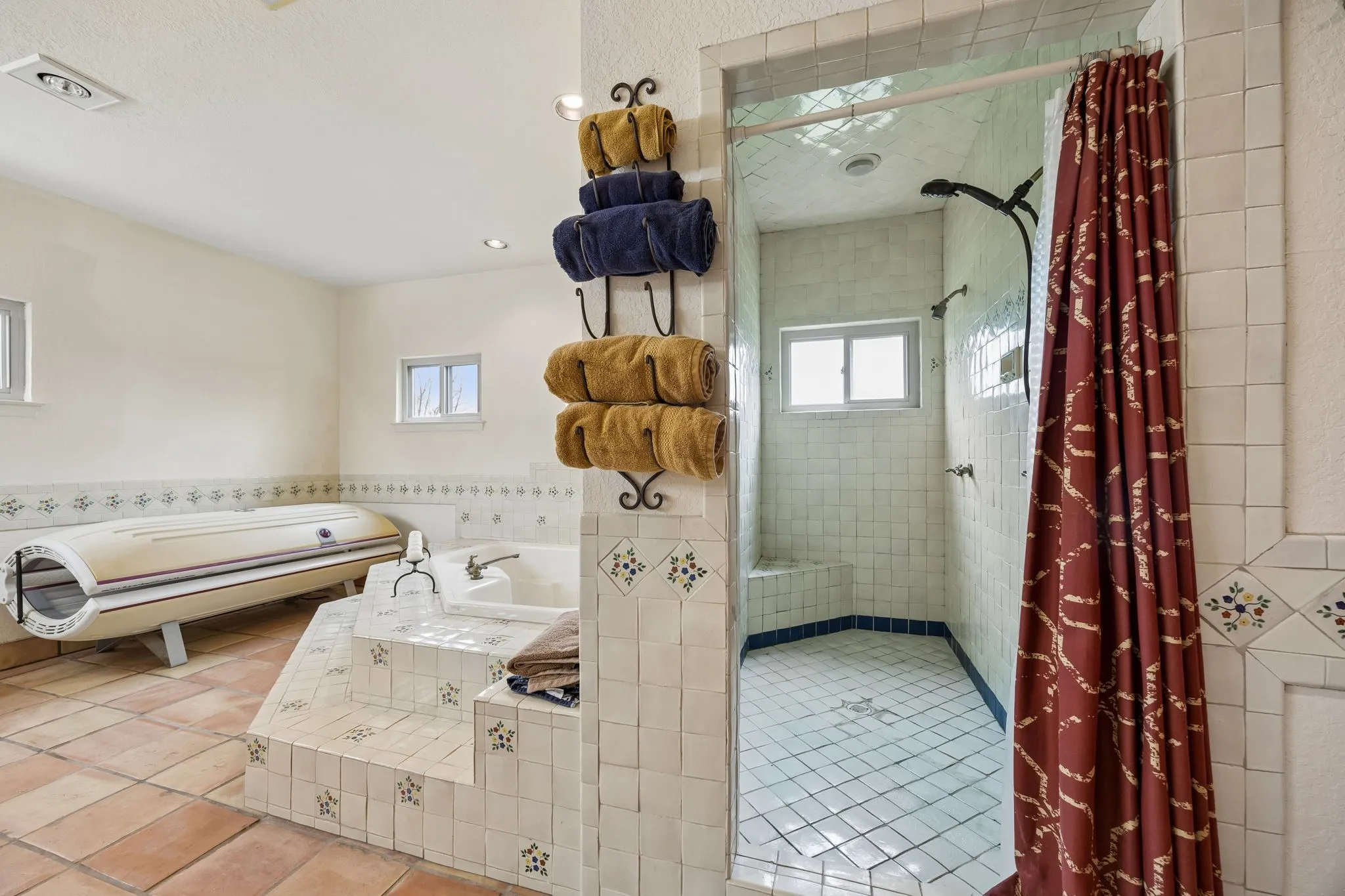 Spacious bathroom featuring a built-in tiled tub with steps, a glass-enclosed shower with a tiled bench, terra cotta style floor tiles, white wall tiles with decorative accents, and recessed lighting