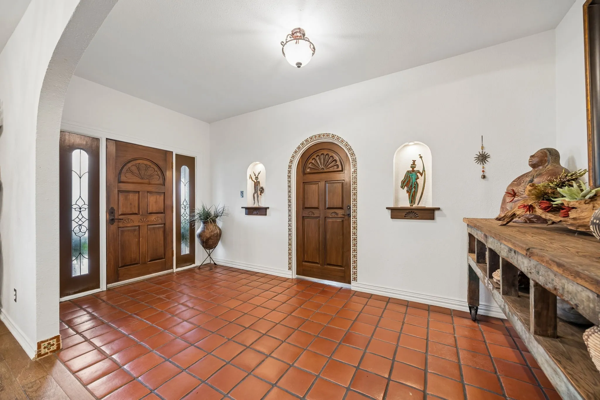 Entryway featuring terracotta tile flooring, a solid wood front door with sidelights, an arched doorway, and built-in wall niches