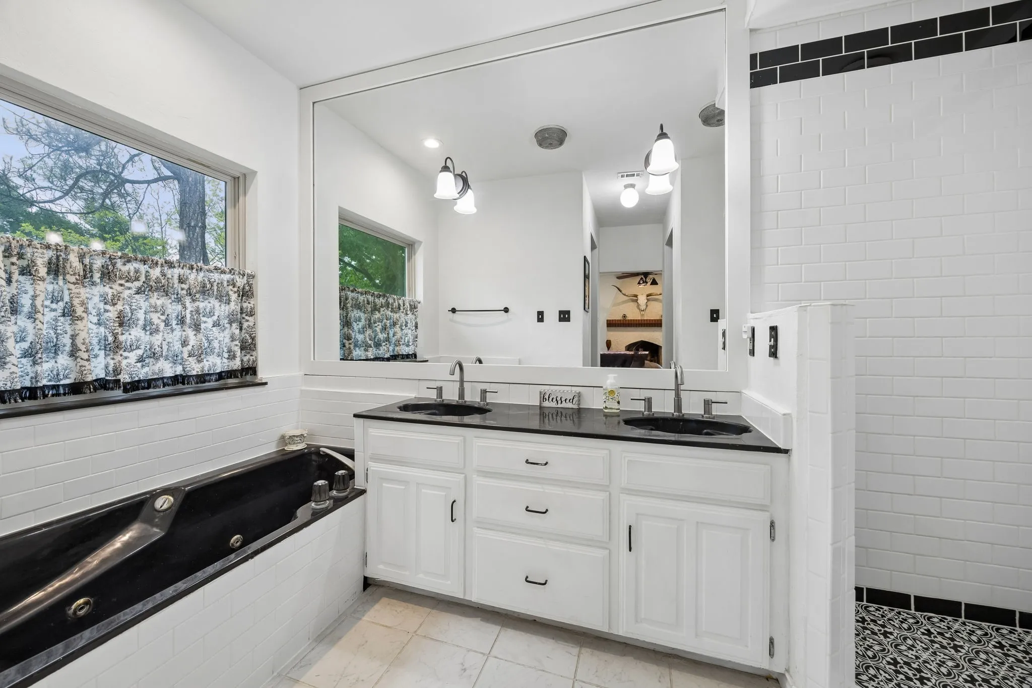 White subway tile bathroom featuring a dual vanity with black sinks and countertops, a black jetted tub, and a shower with patterned black and white floor tiles