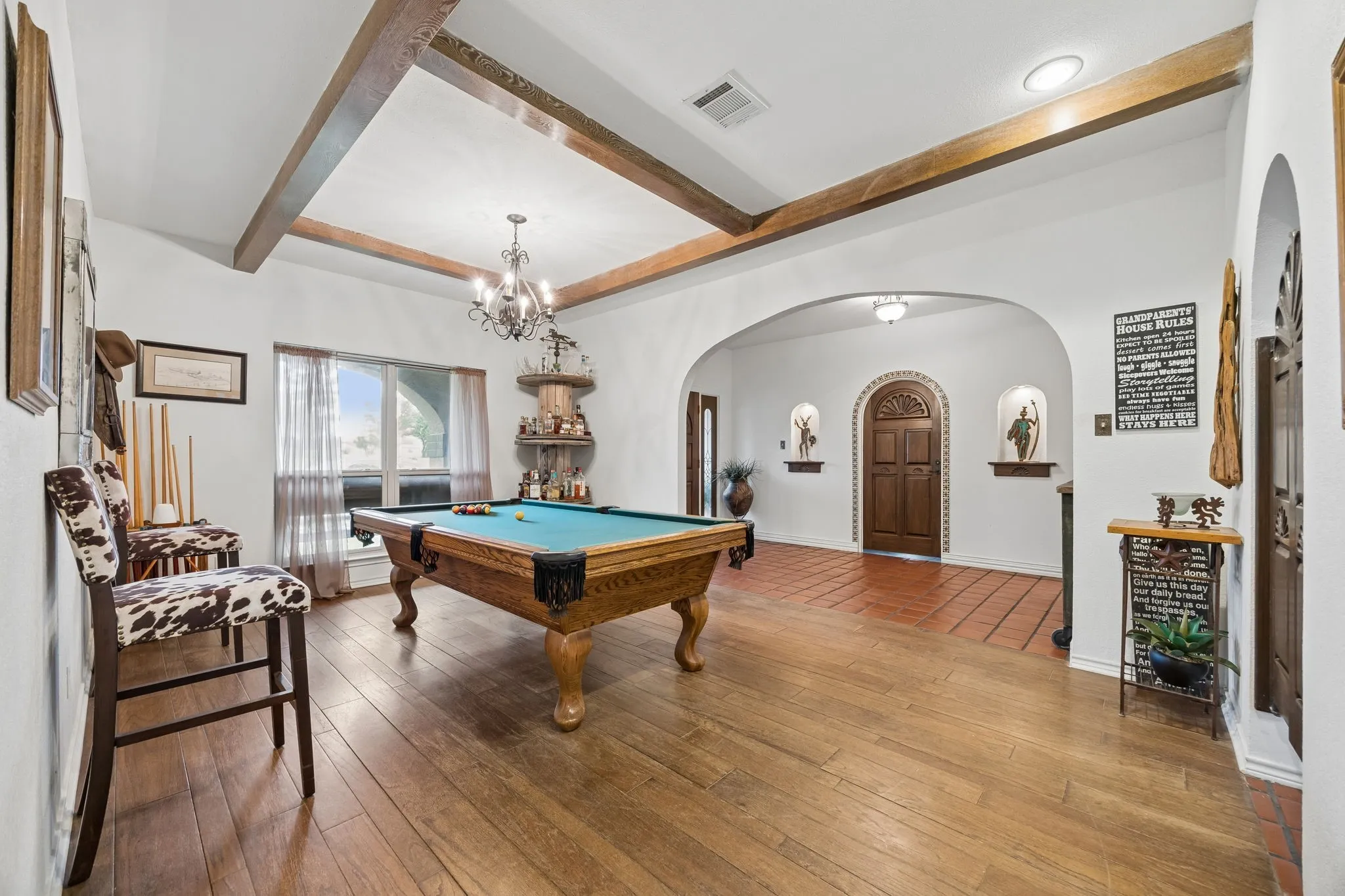 Spacious room featuring wood-finish flooring, exposed ceiling beams, and an arched entryway