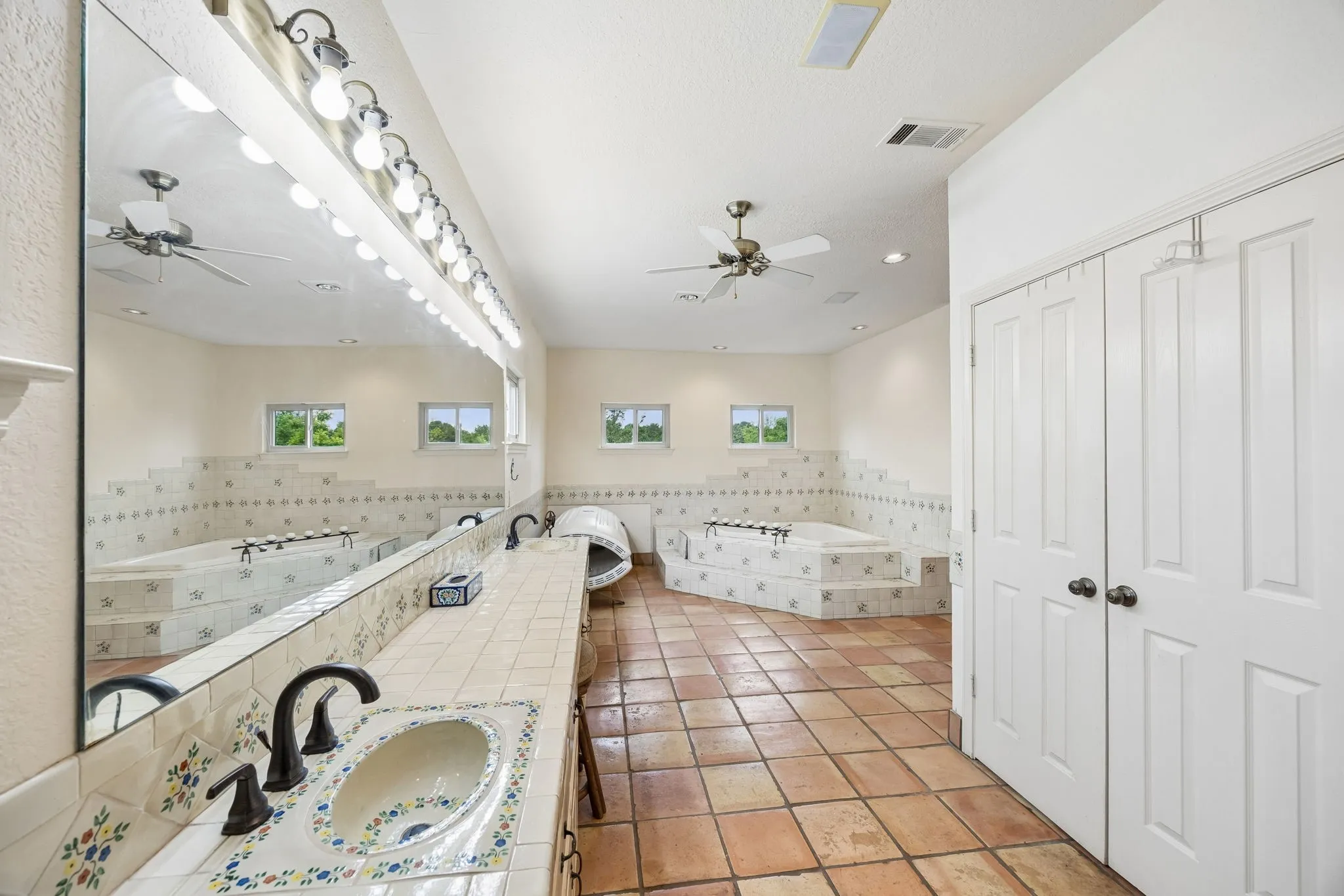 Spacious bathroom featuring terracotta floor tiling, a double vanity with decorative ceramic sinks, and a large mirror with vanity lighting