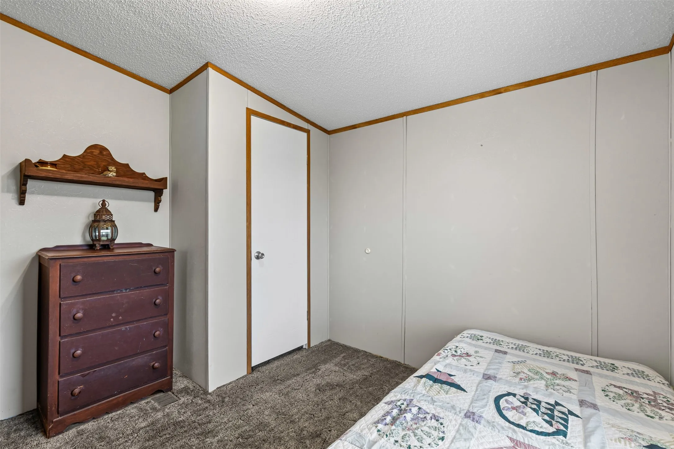 Interior room featuring light-colored wall panels with wood-finish trim, textured ceiling, and gray carpet flooring