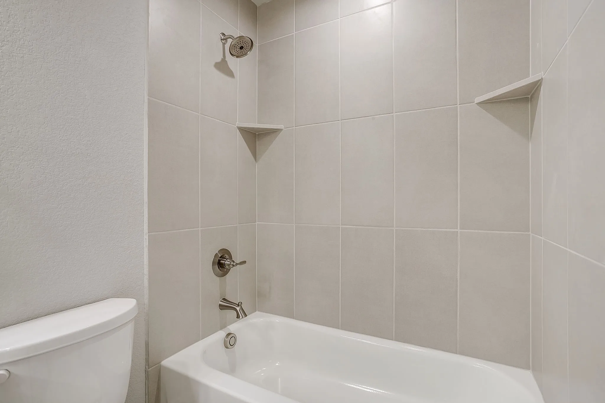 Bathroom with a textured wall and shower / bath combination