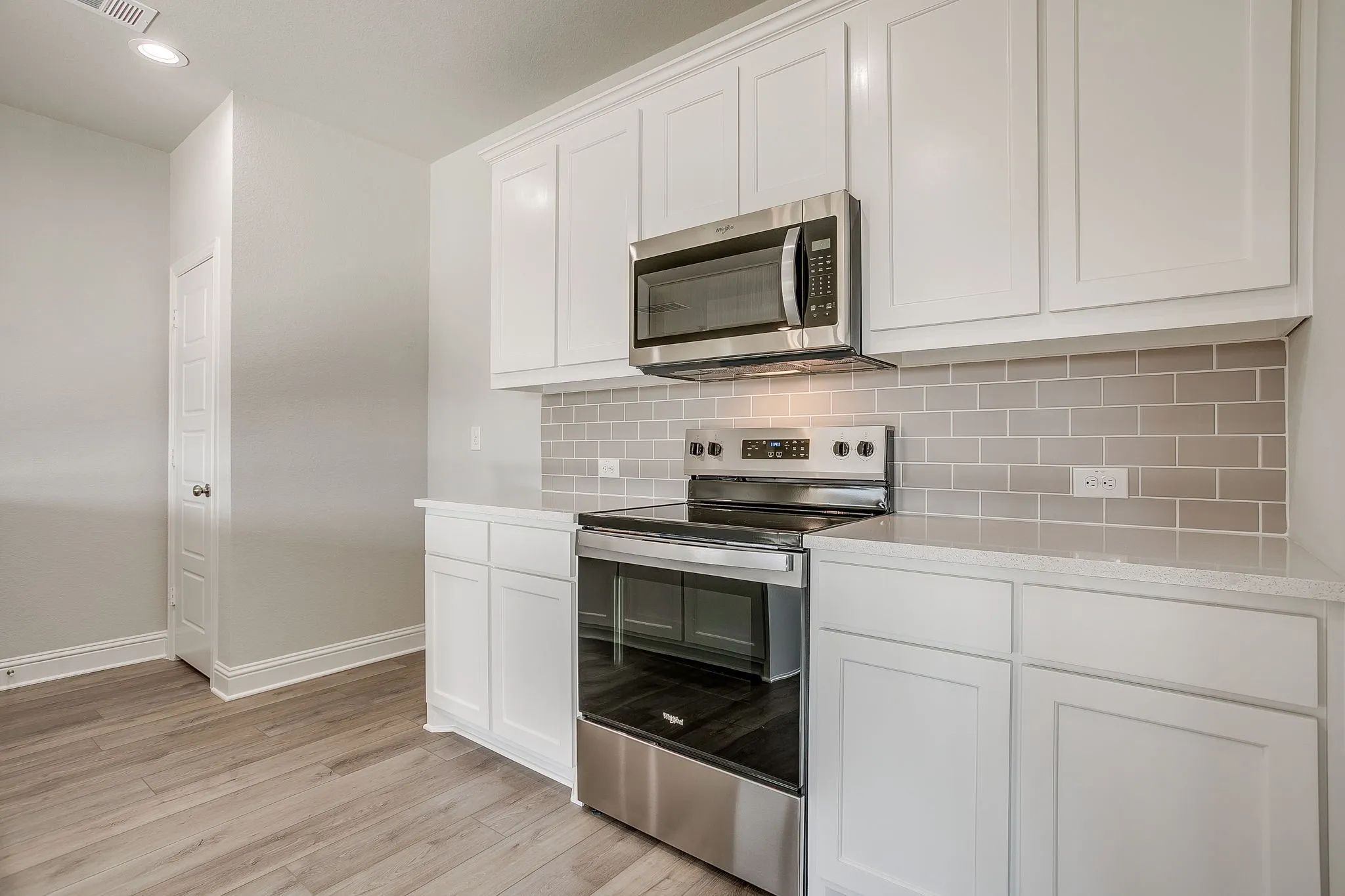 Kitchen with stainless steel appliances, white cabinets, light wood-type flooring, tasteful backsplash, and recessed lighting