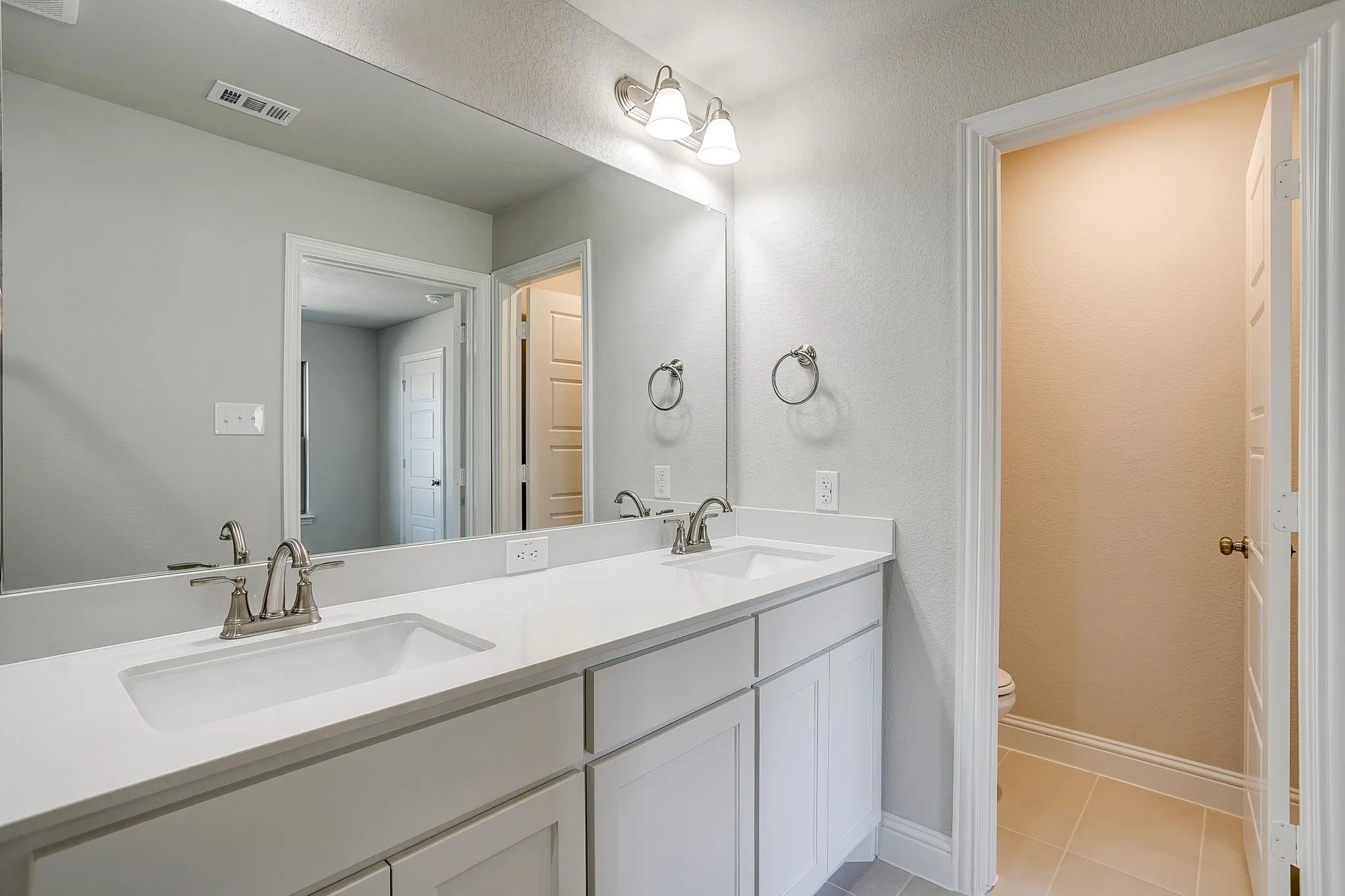 Bathroom featuring double vanity, light tile patterned floors, and a textured wall
