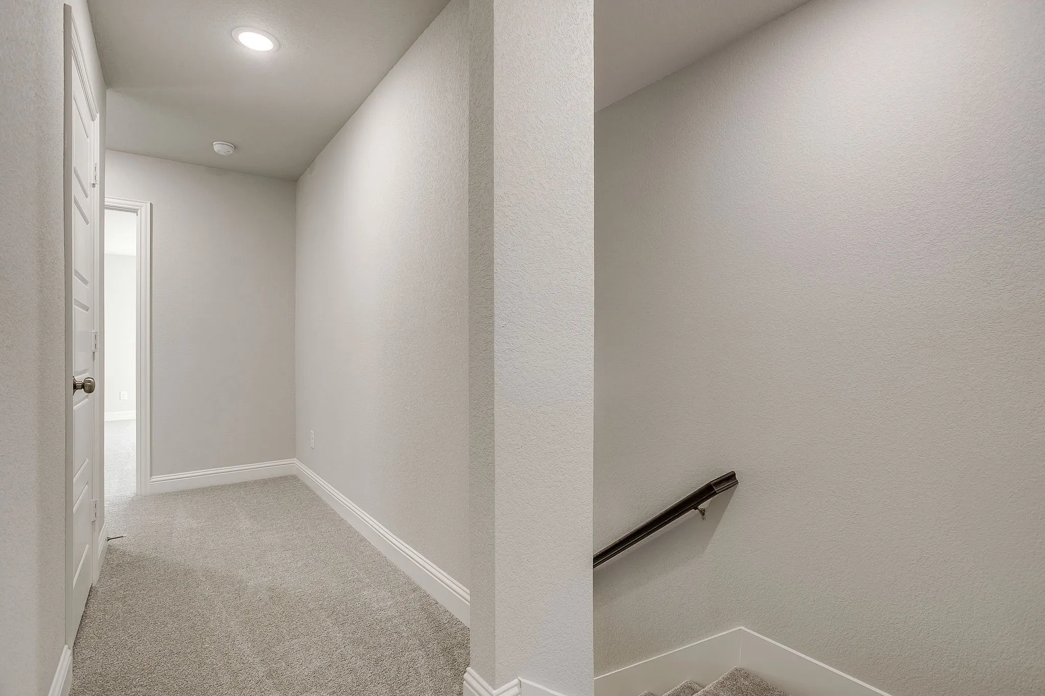 Hall with light carpet, an upstairs landing, a textured wall, and recessed lighting
