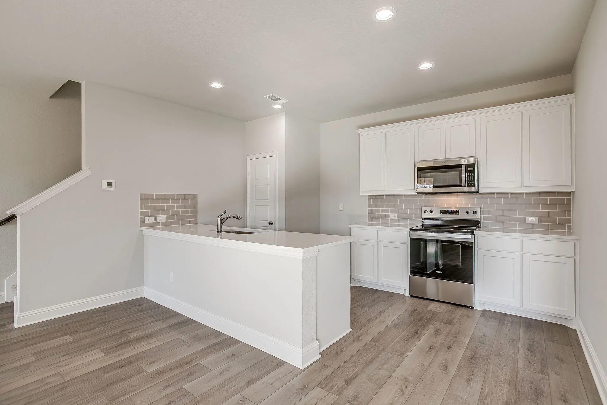Kitchen with stainless steel appliances, white cabinets, a peninsula, light wood finished floors, and recessed lighting