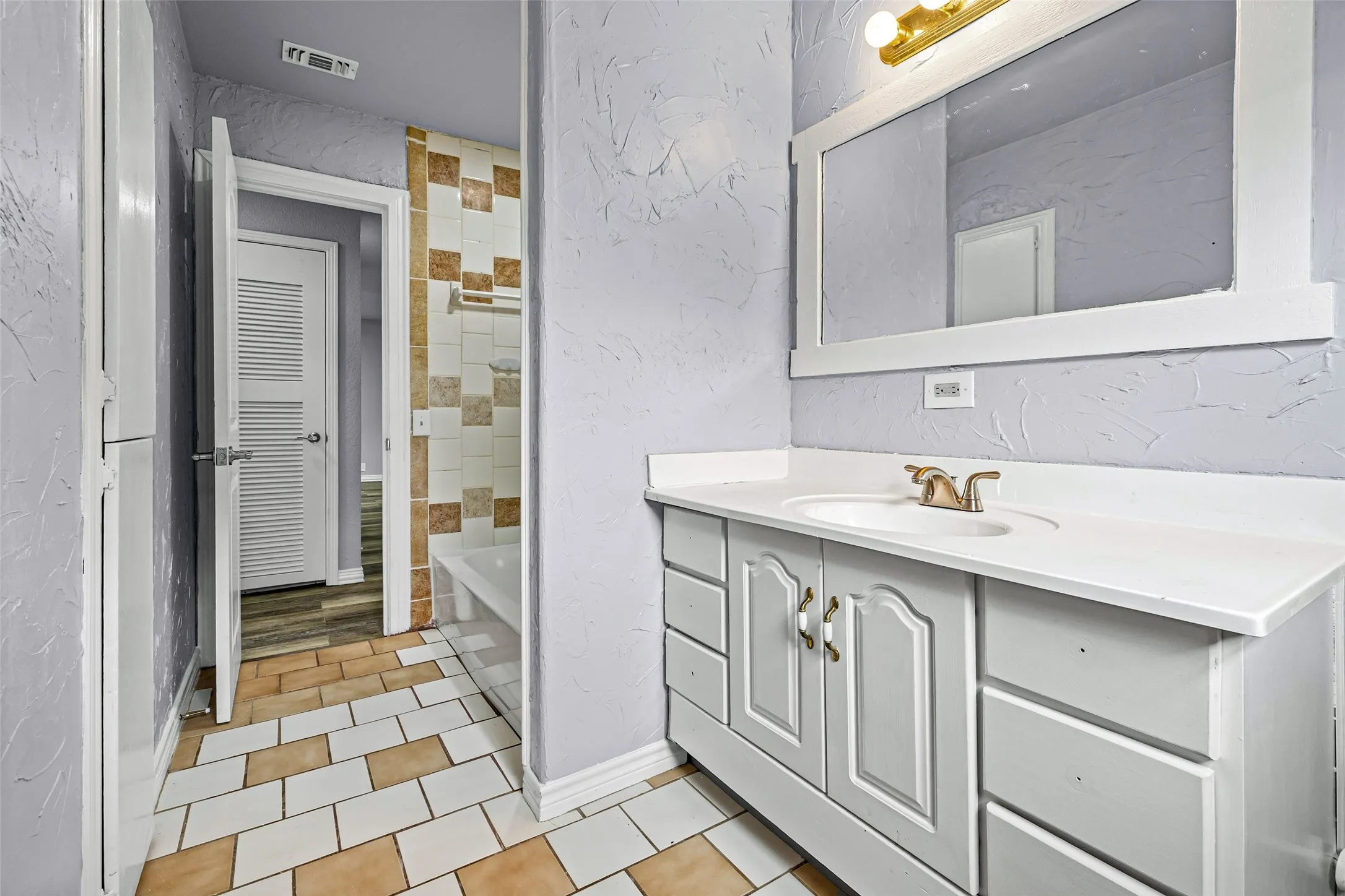 Full bathroom with a textured wall, vanity, a bathtub, and light tile patterned floors