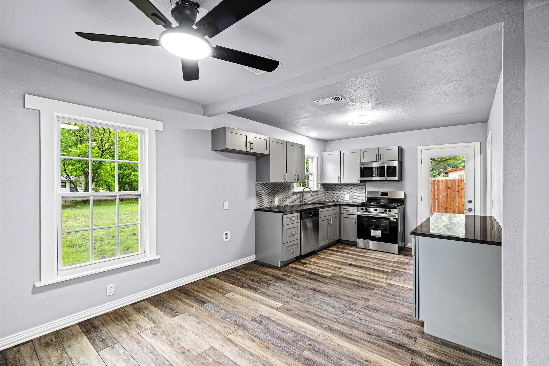 Kitchen featuring gray cabinetry, stainless steel appliances, light wood-style floors, a ceiling fan, and decorative backsplash