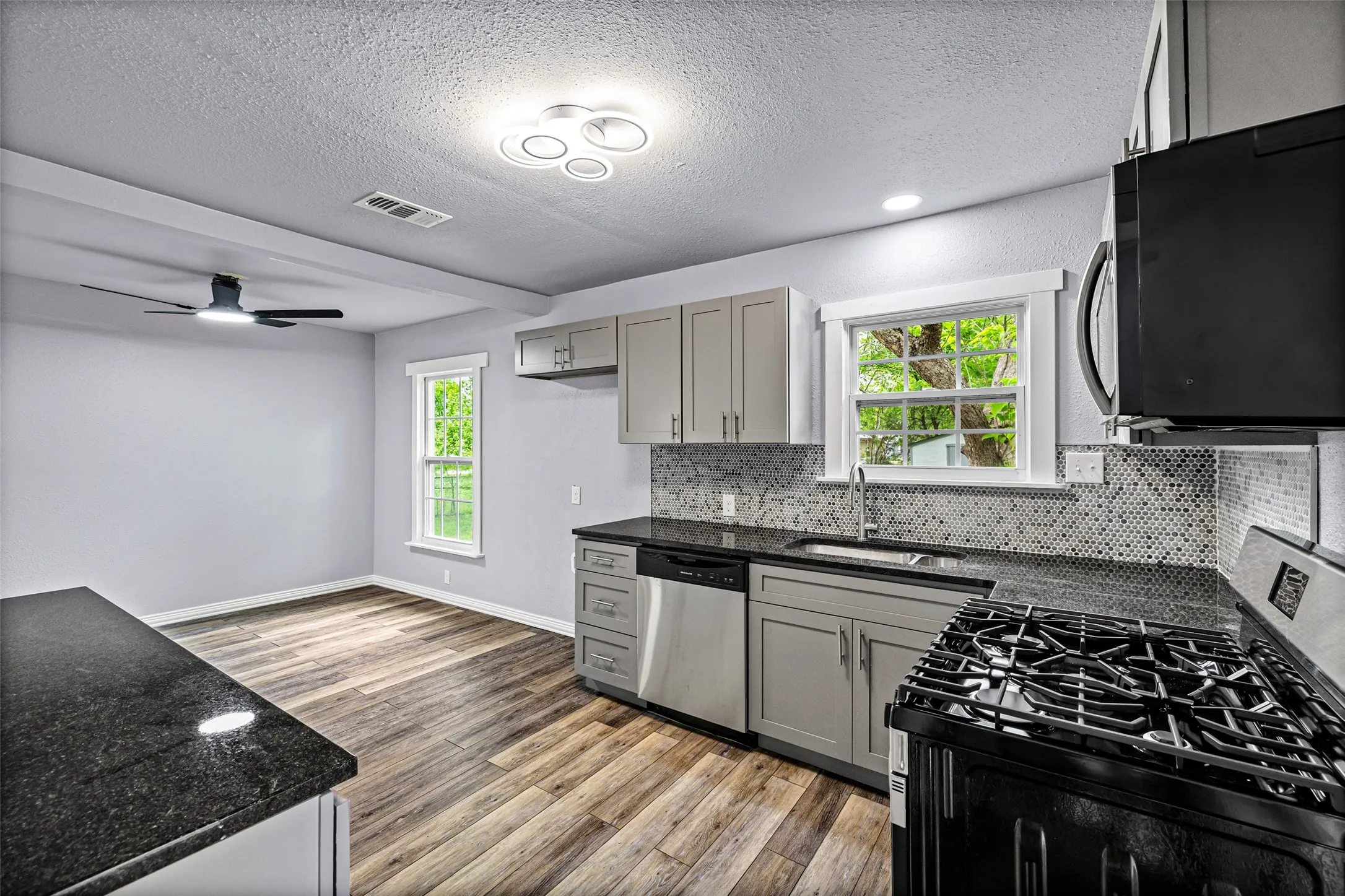 Kitchen with stainless steel appliances, gray cabinetry, tasteful backsplash, light wood-style floors, and a textured ceiling