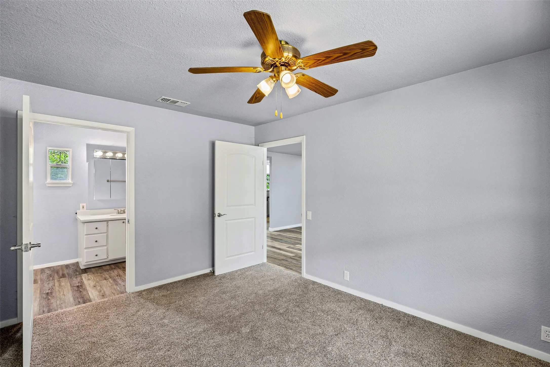 Unfurnished bedroom featuring carpet, connected bathroom, a textured ceiling, and a ceiling fan