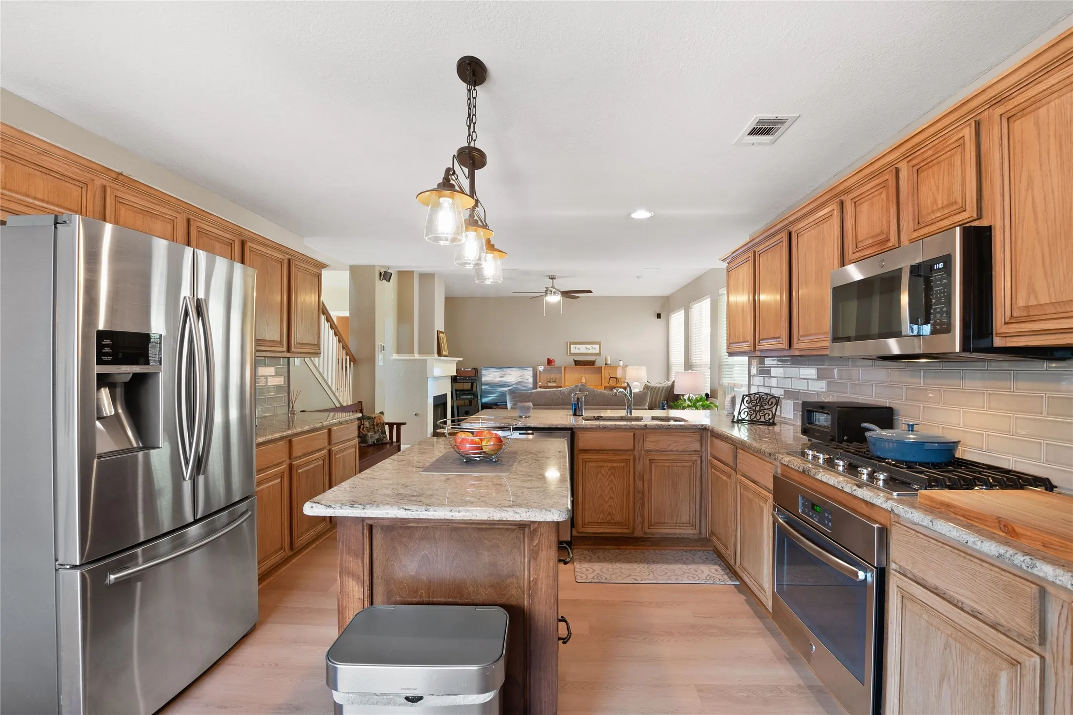 Kitchen featuring light wood-finish cabinetry, stainless steel appliances, speckled countertops, and a subway tile backsplash