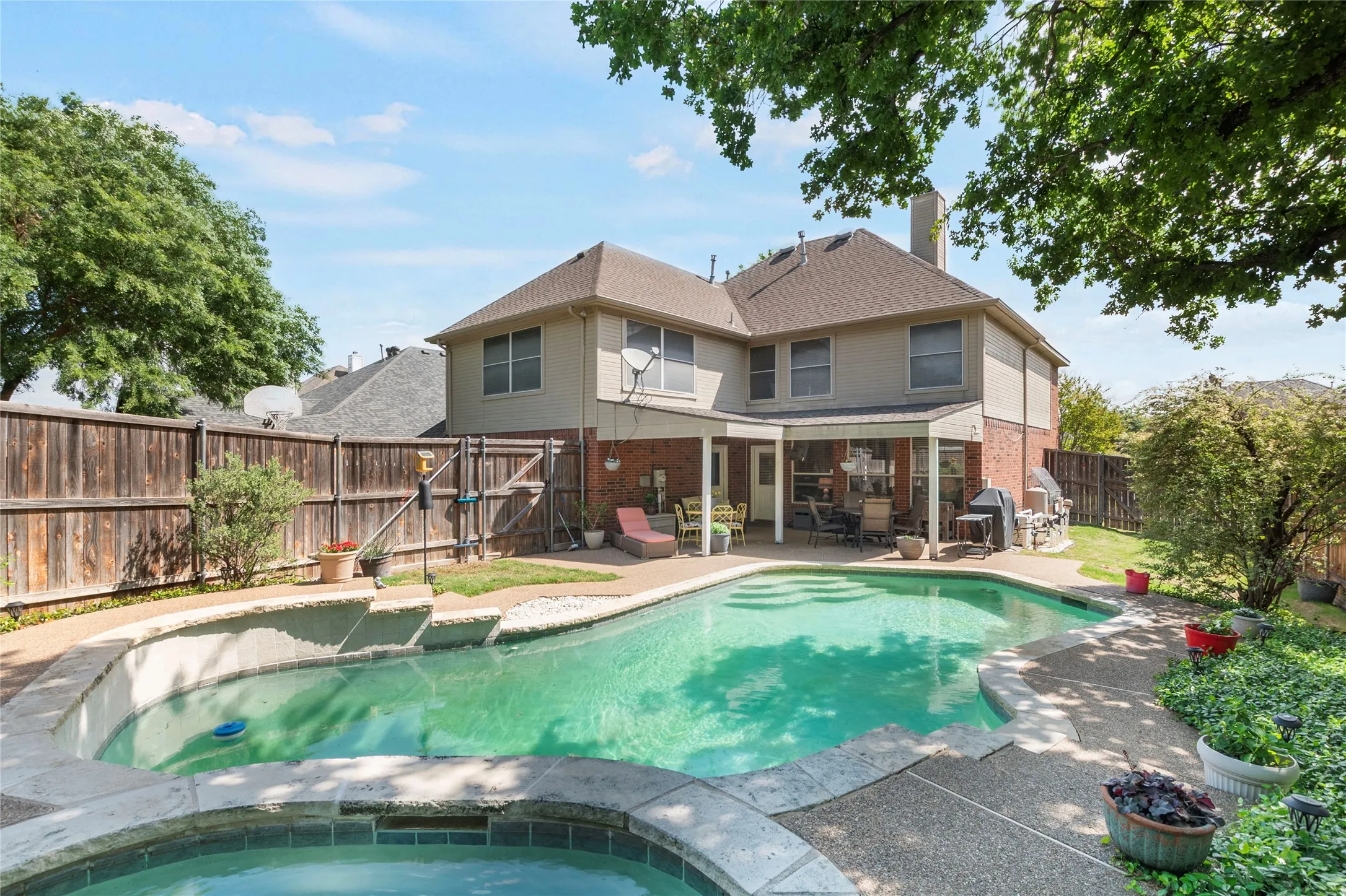 Rear view of property featuring a patio area, a fenced backyard, brick siding, a chimney, and an in-ground hot tub