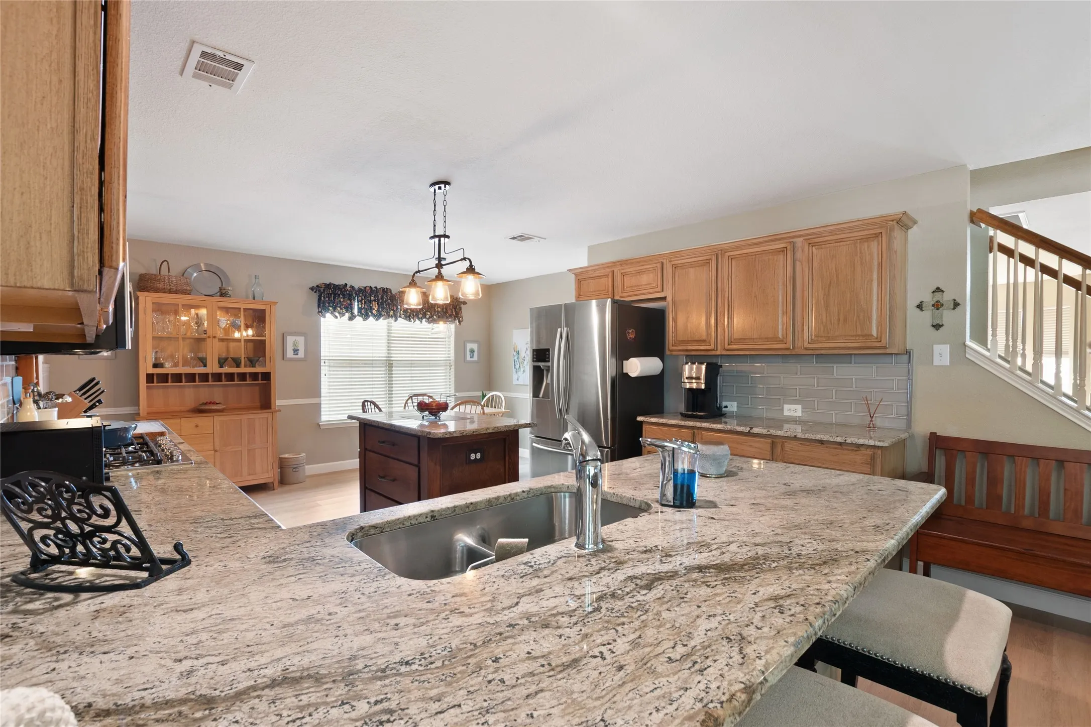 Kitchen featuring granite countertops, wood-finish cabinetry, stainless steel appliances, a center island with additional storage, and an updated light fixture