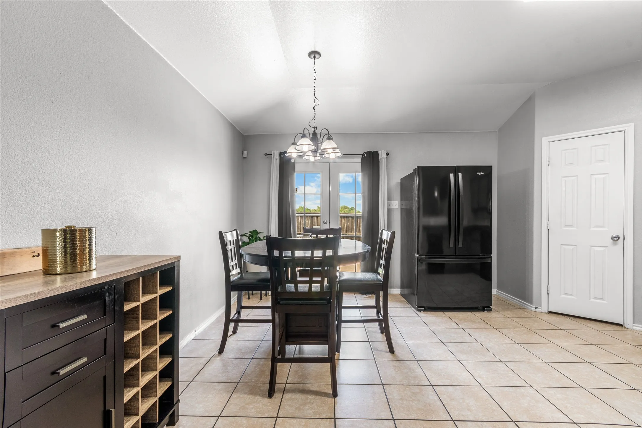 This dining area features tile flooring, a black refrigerator, and a door leading to an exterior space