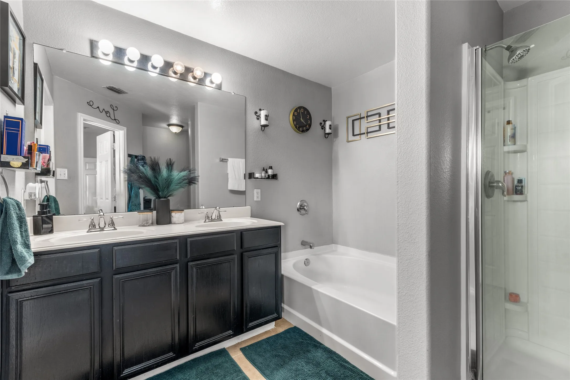 Bathroom featuring a double vanity with two sinks, dark cabinetry, and a large mirror with overhead lighting