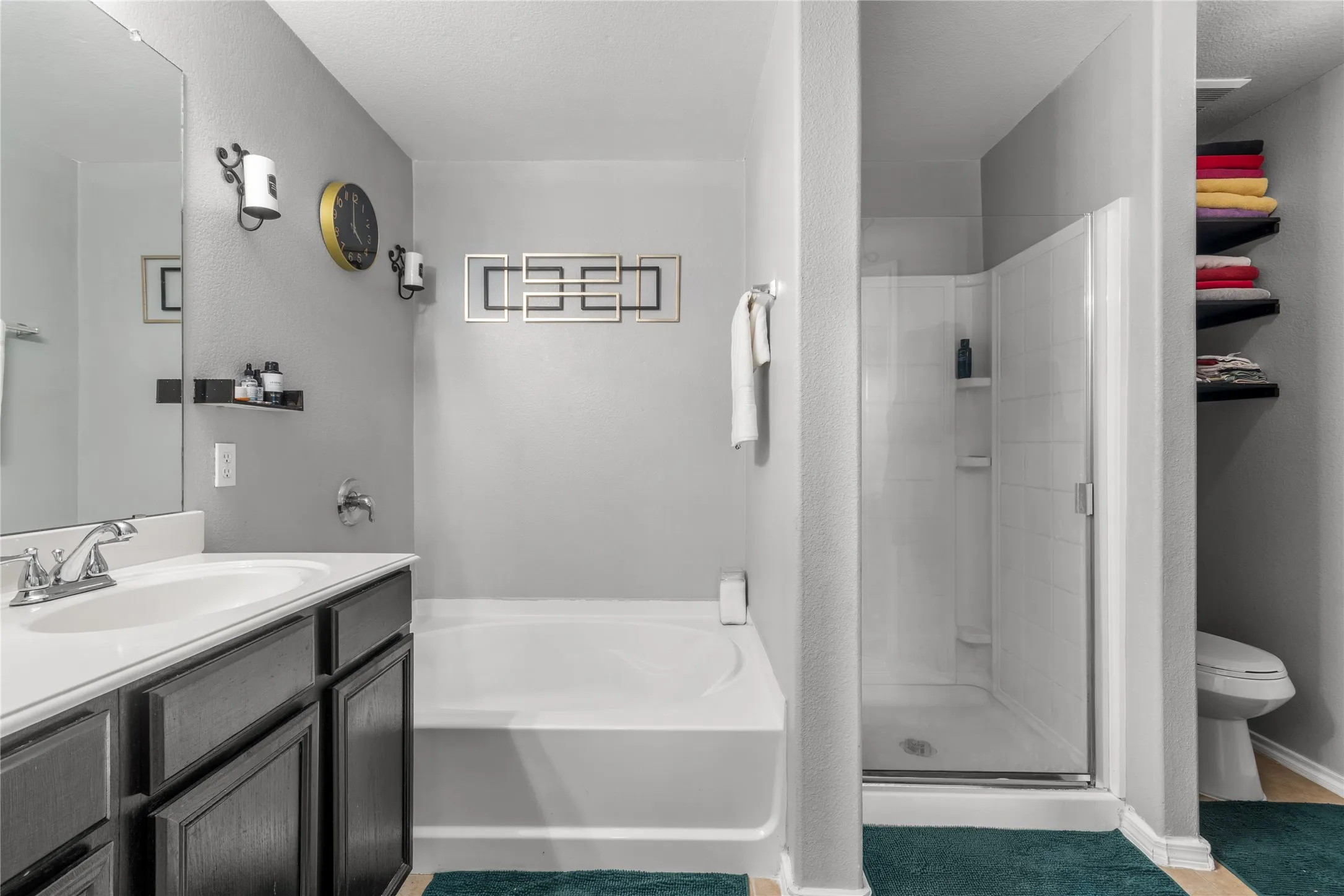 Bathroom featuring a white bathtub, a walk-in shower with a glass enclosure, a single vanity with dark cabinetry and a white countertop, and shelving