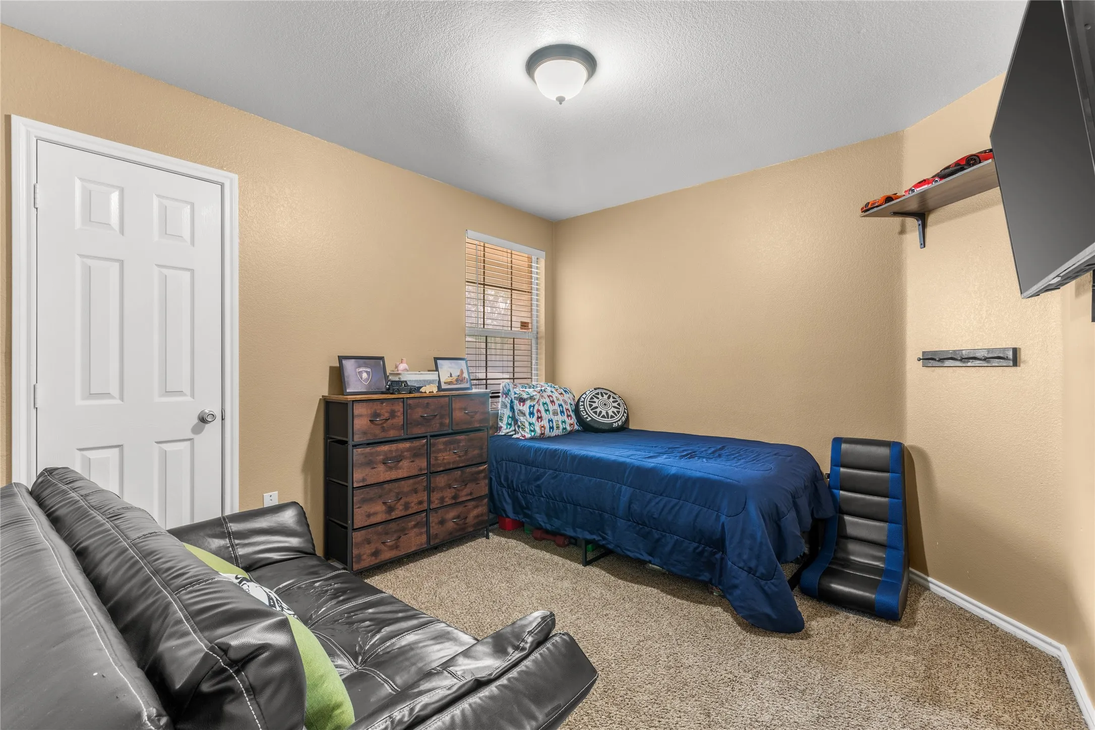 This room features carpeting, a window with blinds, and a white door with a round knob