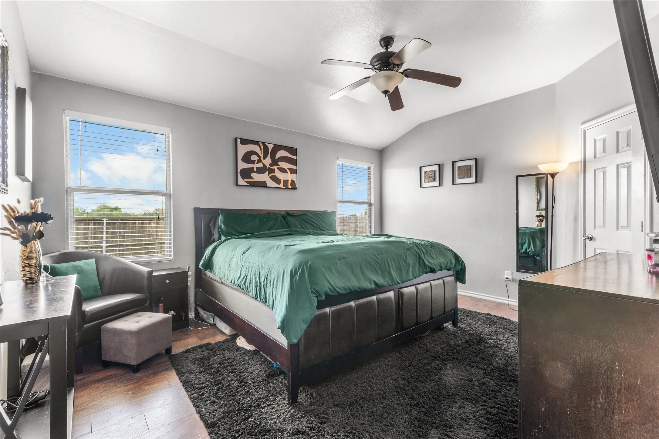 This bedroom features vaulted ceilings, a ceiling fan, and windows with horizontal blinds