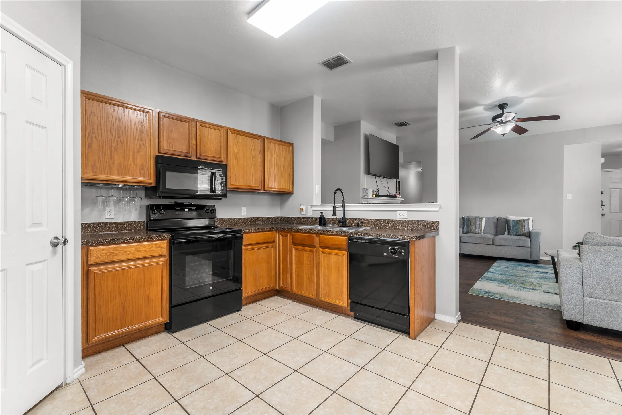 The kitchen features wood cabinetry, black appliances, and durable tile flooring