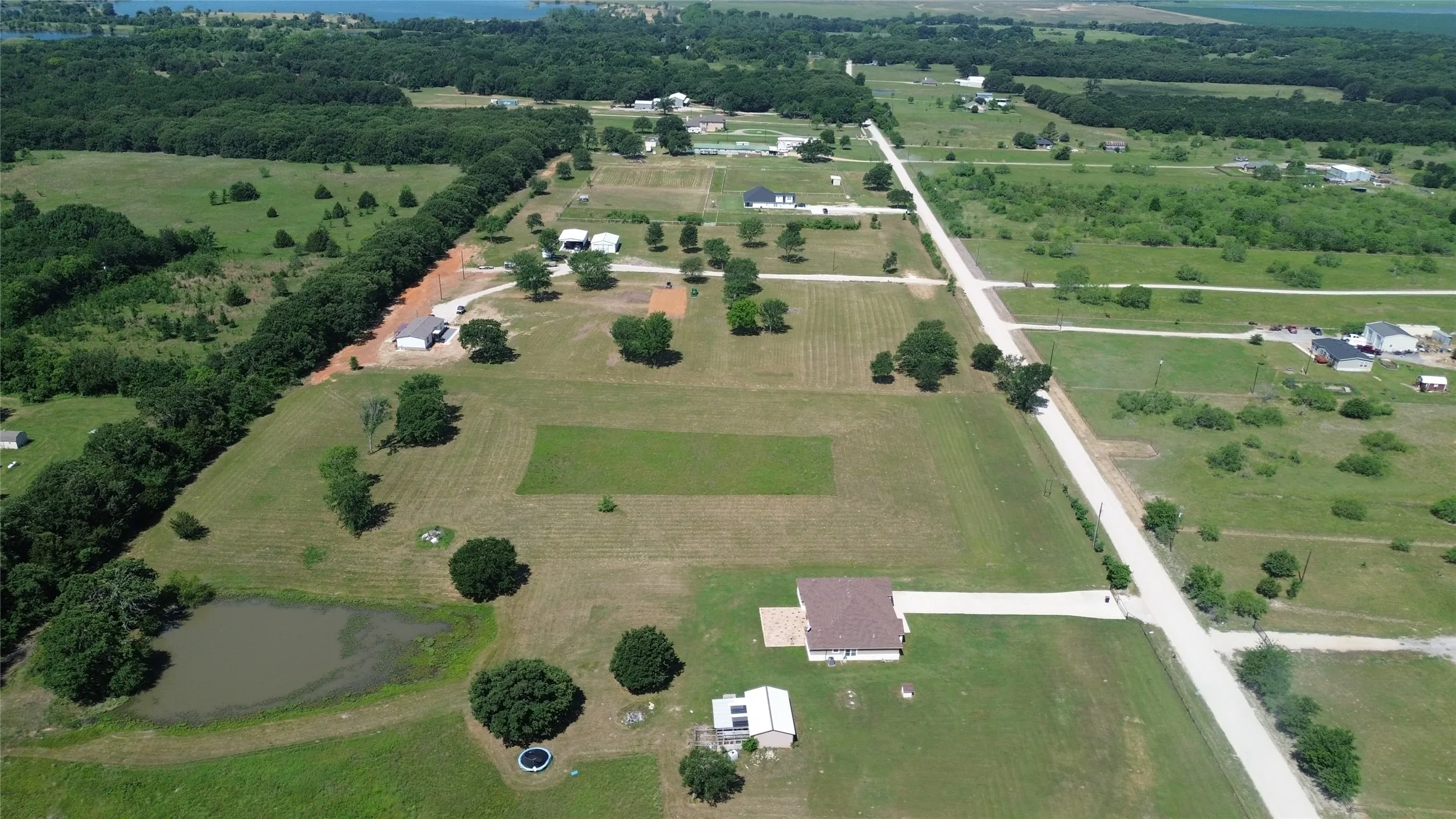 Expansive property featuring a single-story residence with a brown shingle roof, a private pond, and a gravel driveway