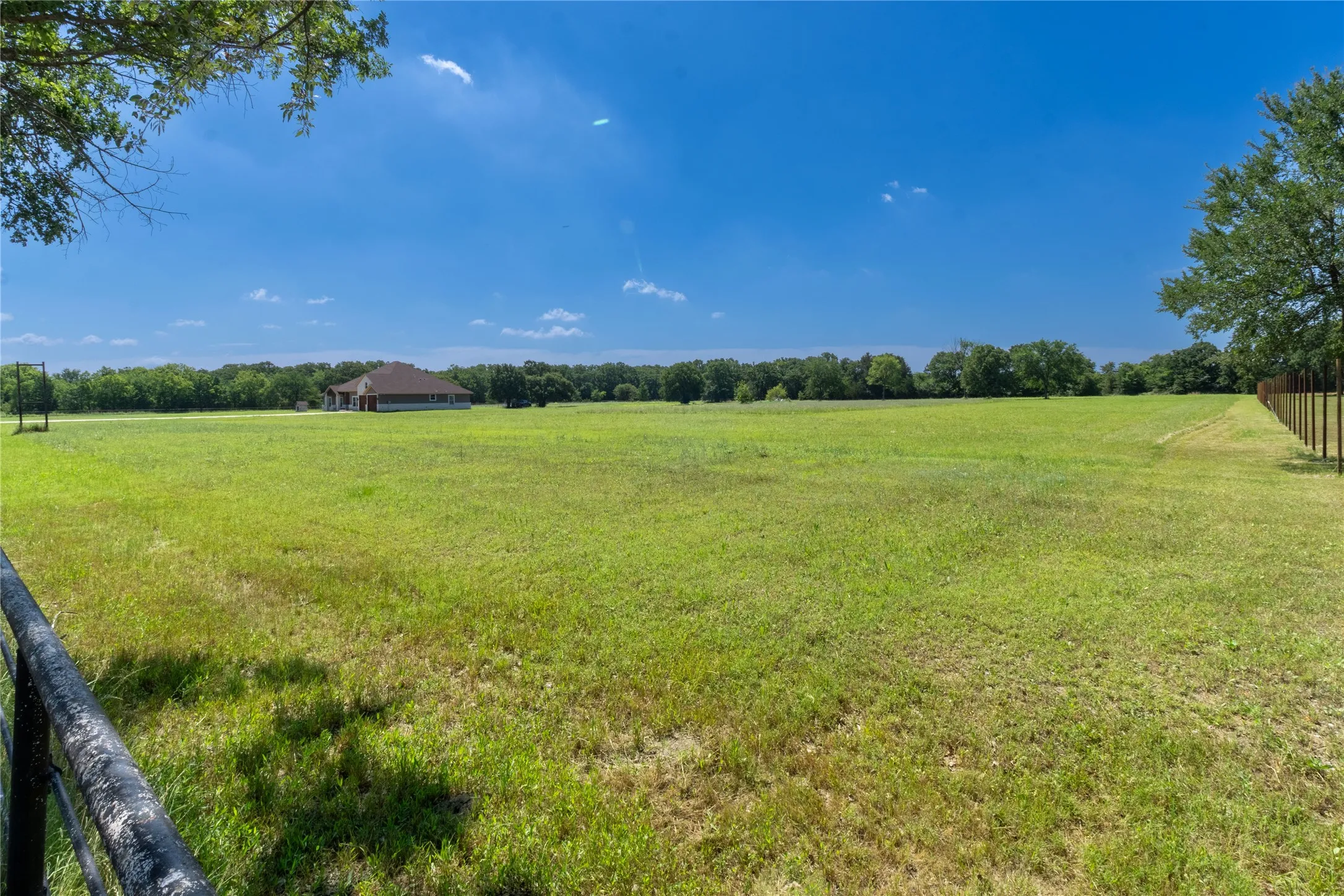 Expansive green pasture with a distant single-story property featuring a brick exterior and a brown shingle roof