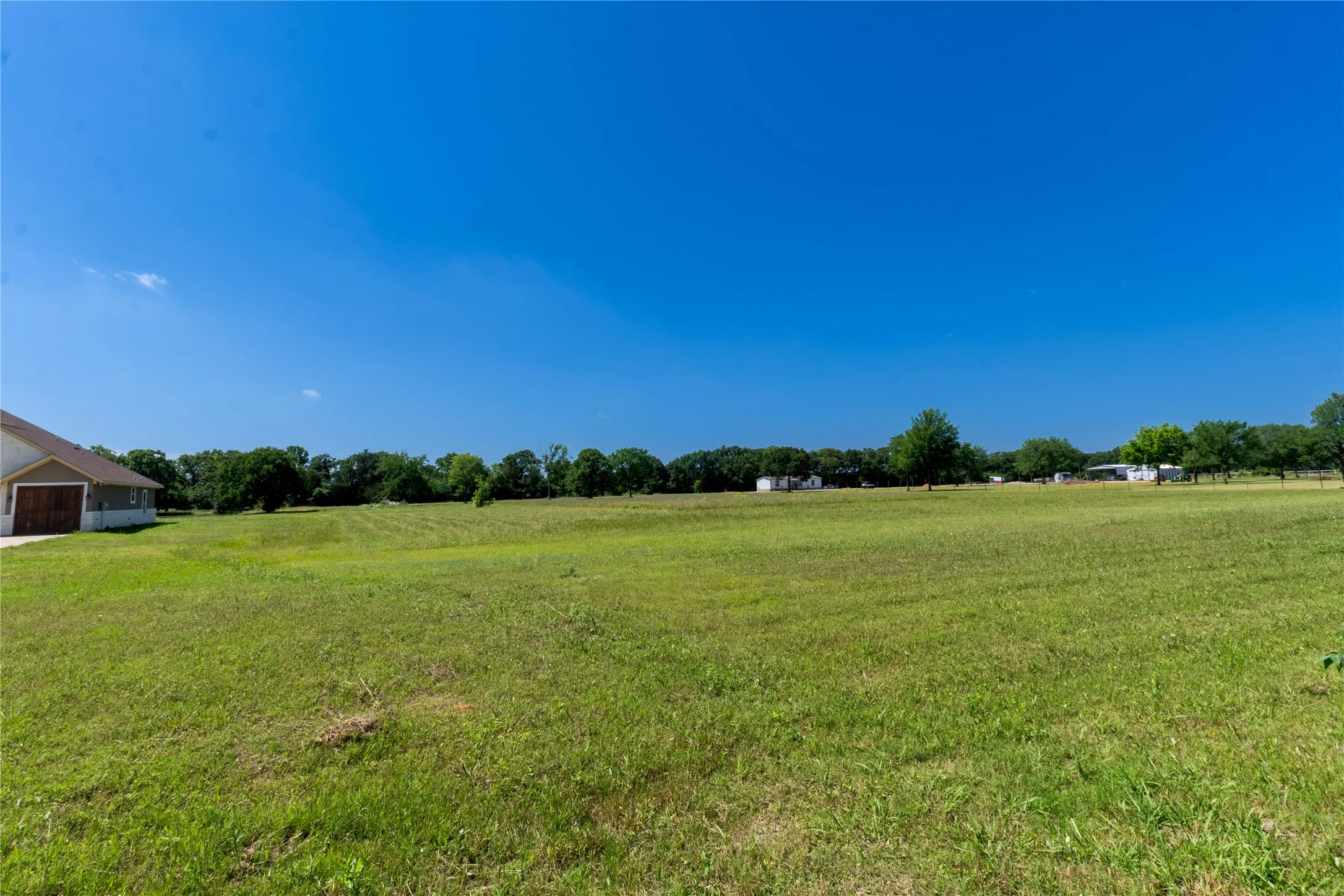 Expansive green space featuring a large field, mature trees lining the perimeter, and a clear blue sky overhead