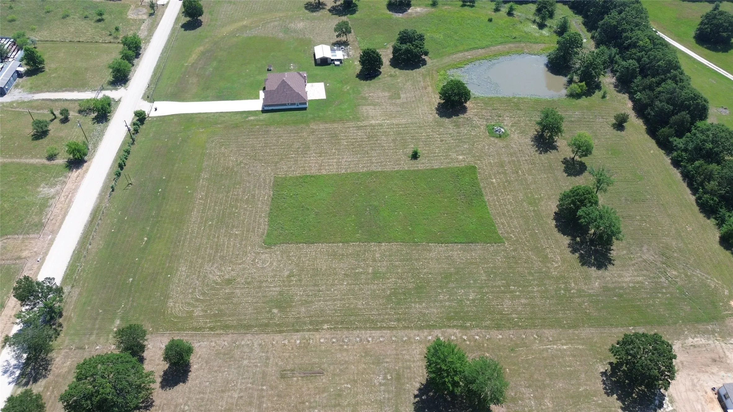 Expansive lot featuring a single-story residence with a brown shingle roof, a long concrete driveway, and a partially wooded perimeter